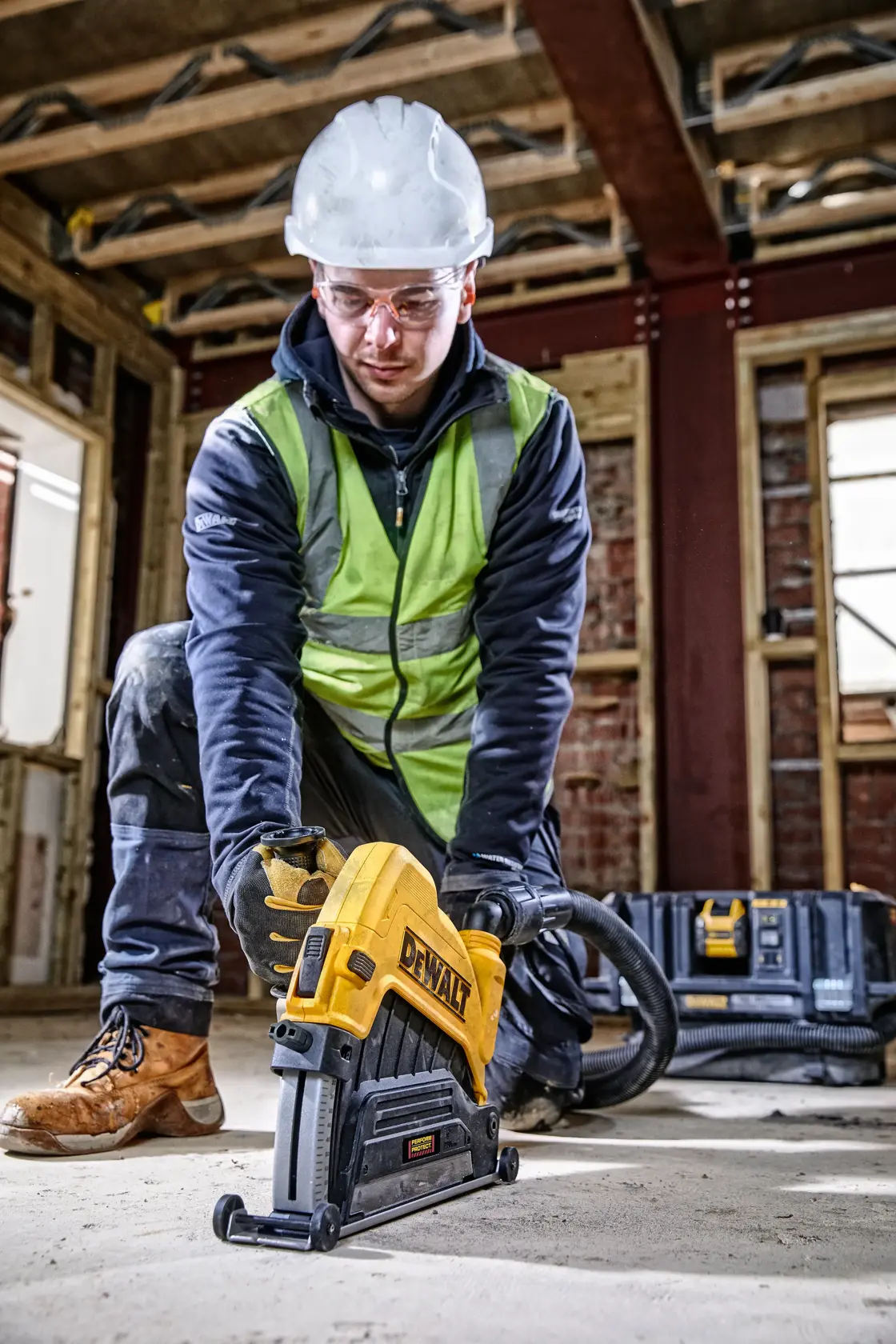 Operaio usa utensile DEWALT sul pavimento, indossa dispositivi di sicurezza e guanti.