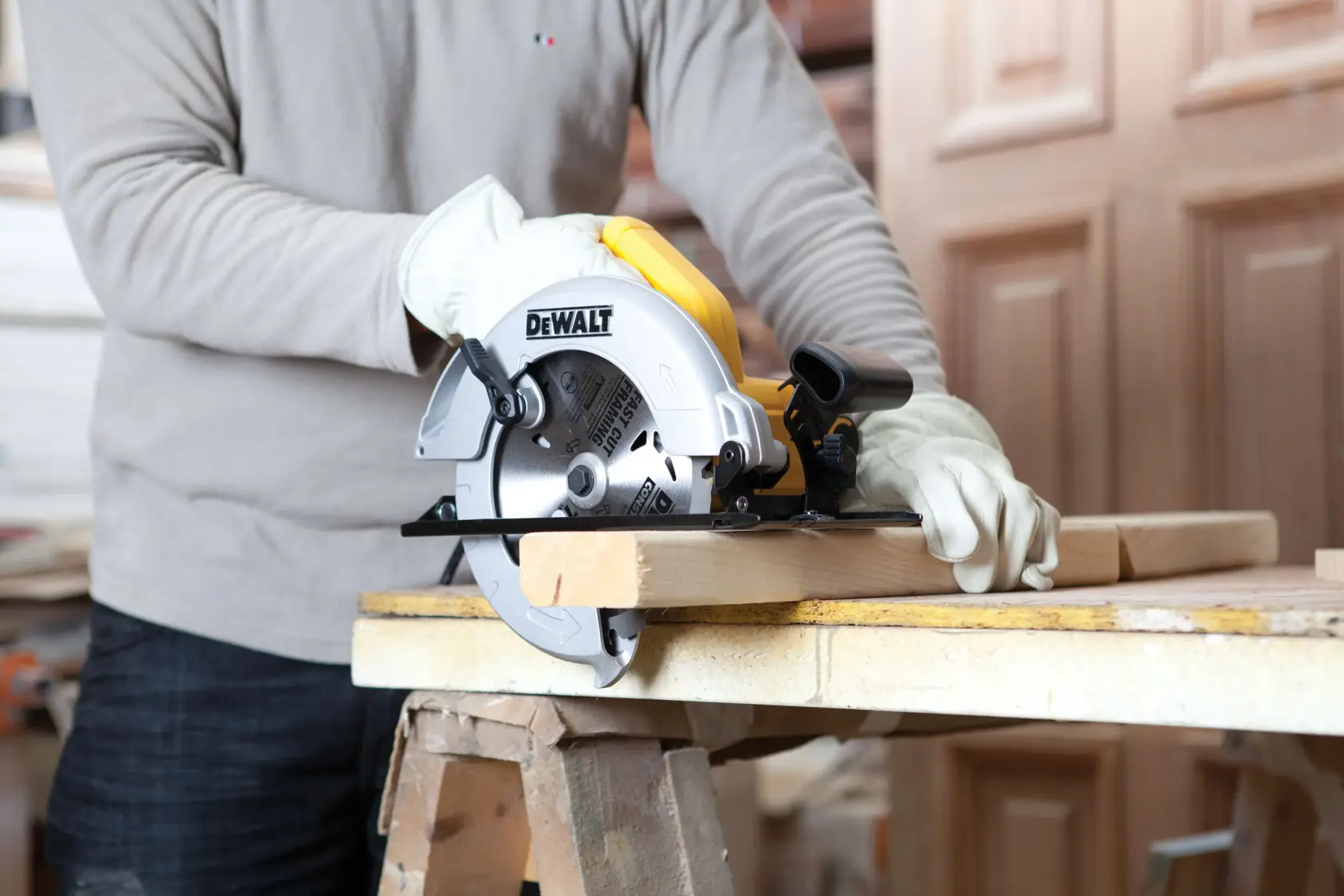 A person wearing gloves is using a DEWALT circular saw (model DWE560) to cut a wooden plank on a workbench.