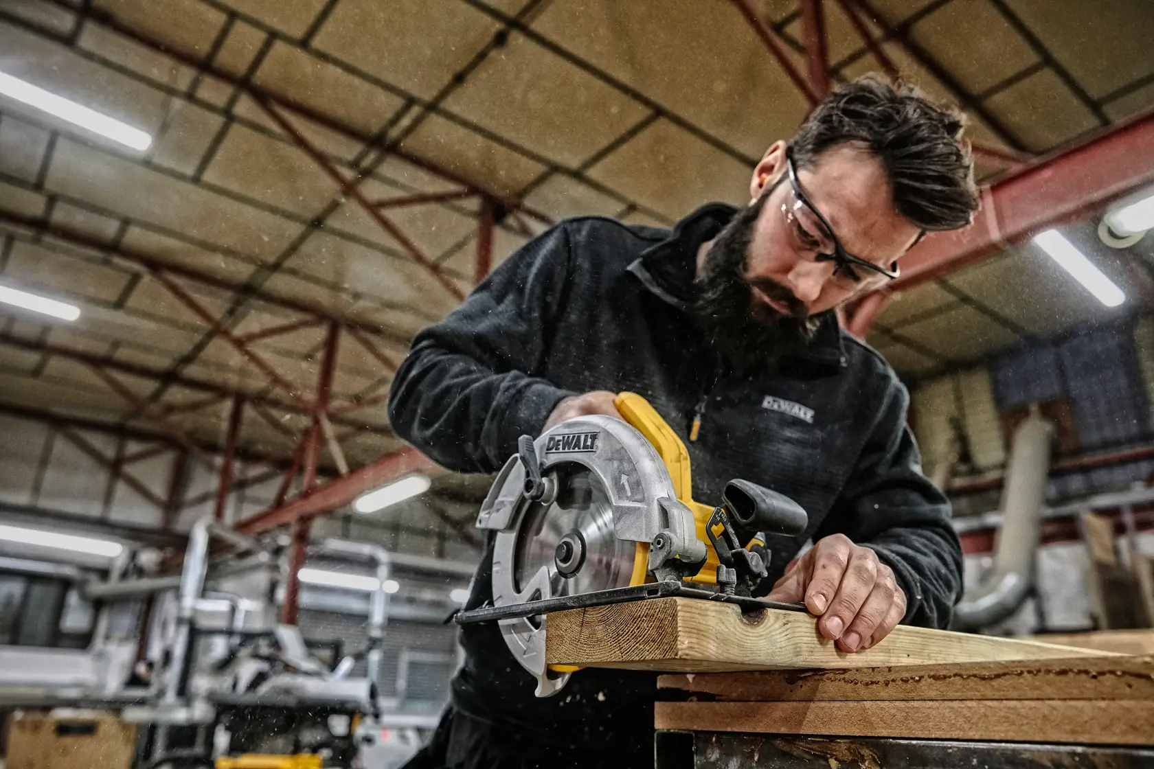 Person using a DEWALT DWE560 circular saw to cut wood in a workshop. Face is blurred for privacy.