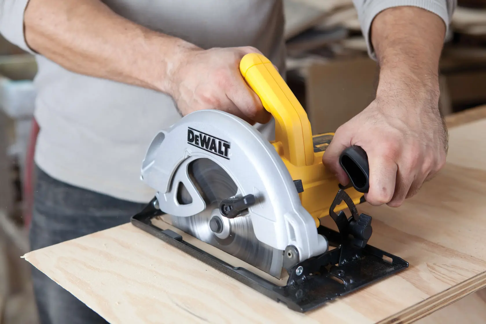 A person using a DEWALT DWE560 circular saw to cut a piece of wood. The tool features a yellow handle and a silver blade housing.