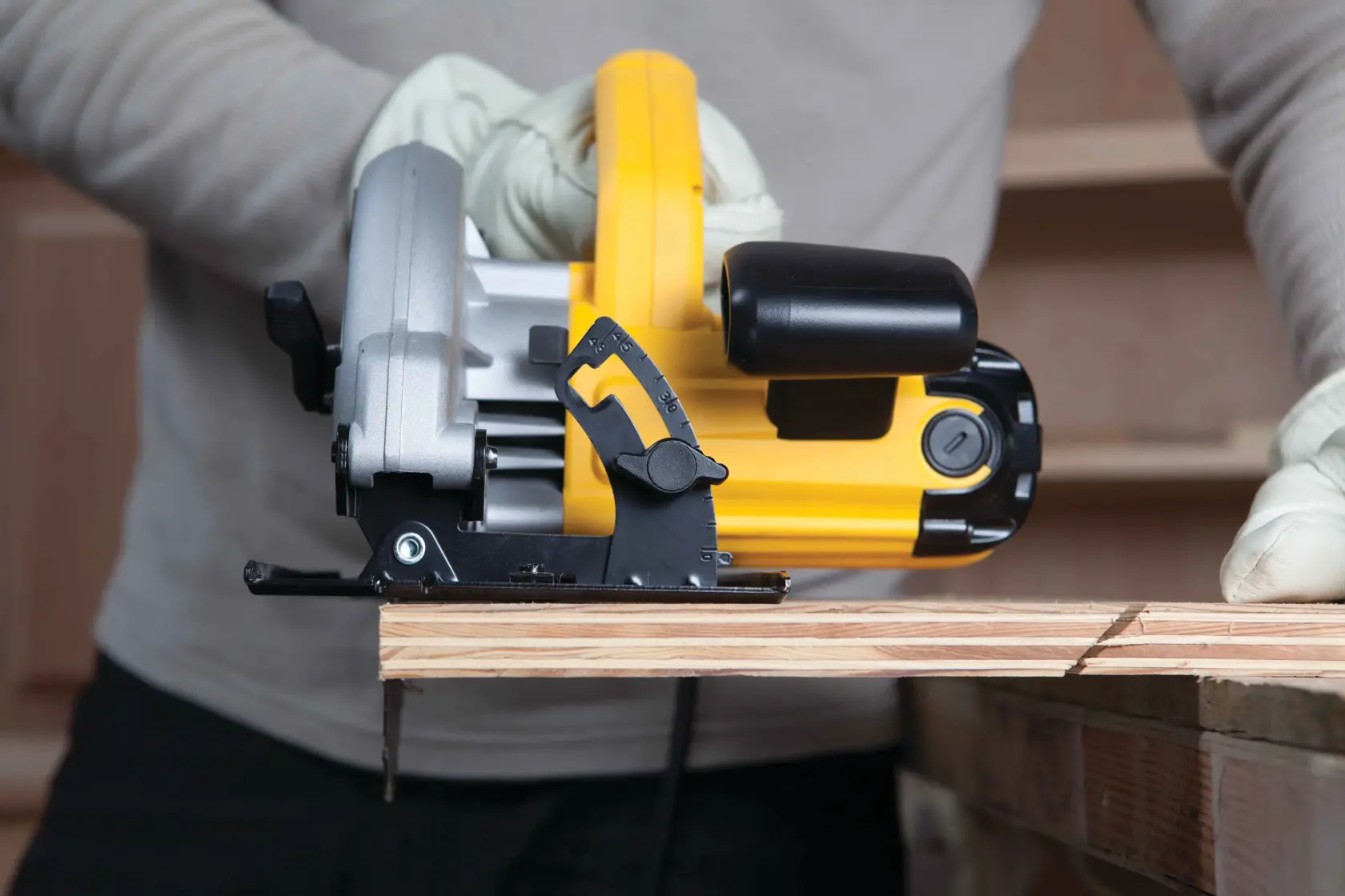 A person wearing gloves is using a yellow and black DEWALT circular saw to cut a piece of wood.