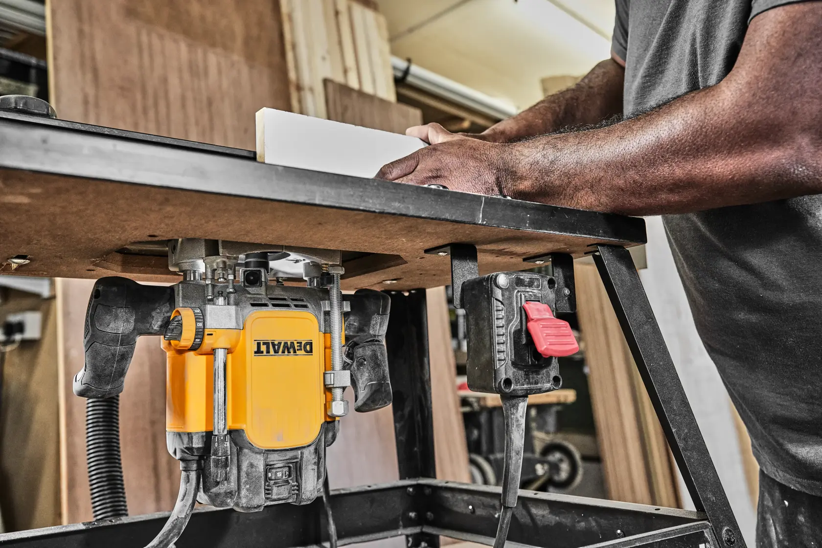 DEWALT router mounted on a workbench in use, with hands guiding a piece of wood in a workshop setting.