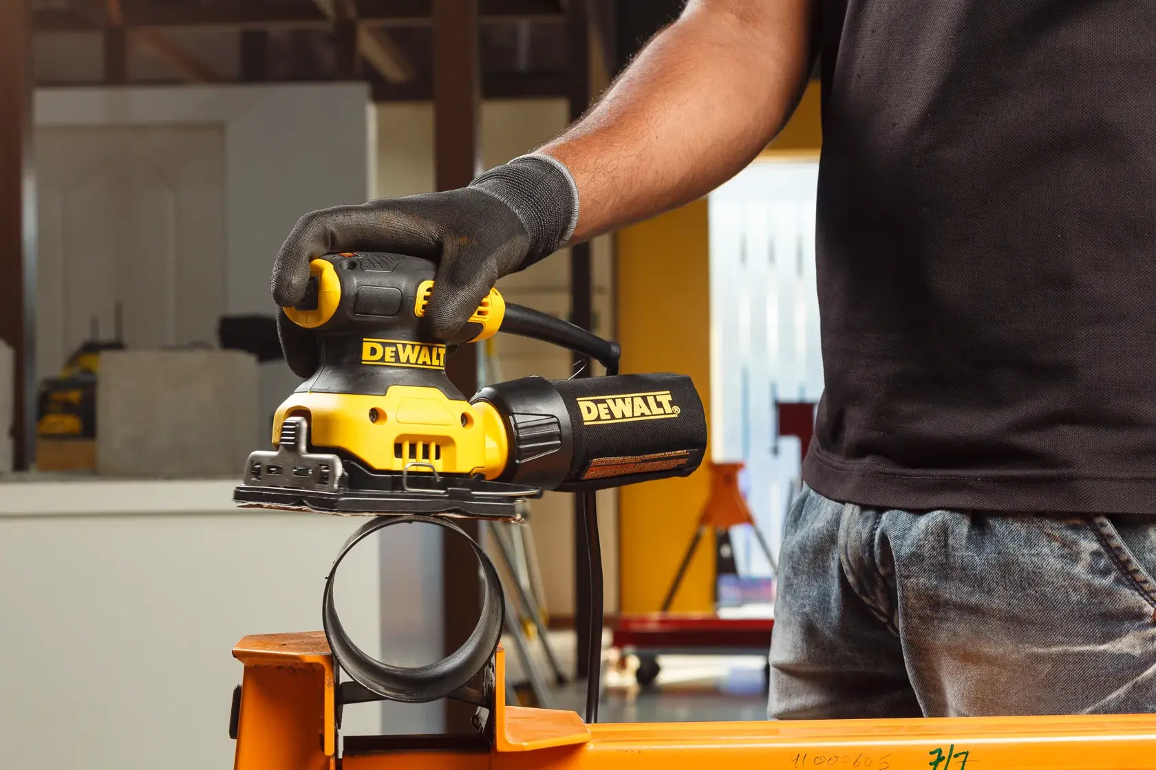 Hands connecting a hose to a yellow DEWALT power tool, used for woodworking or sanding.