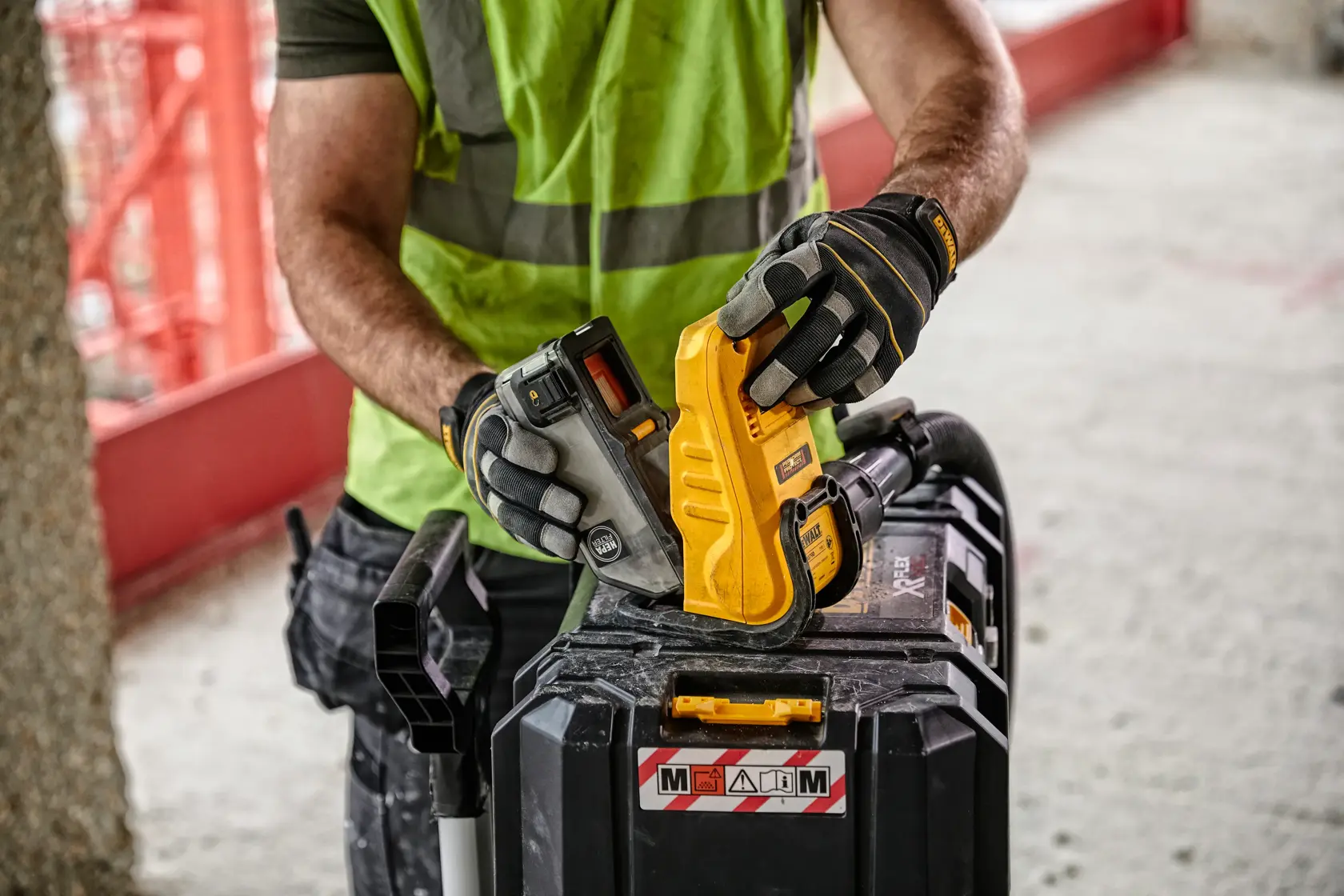 Worker in gloves handling a DEWALT tool with a battery on a jobsite toolbox.