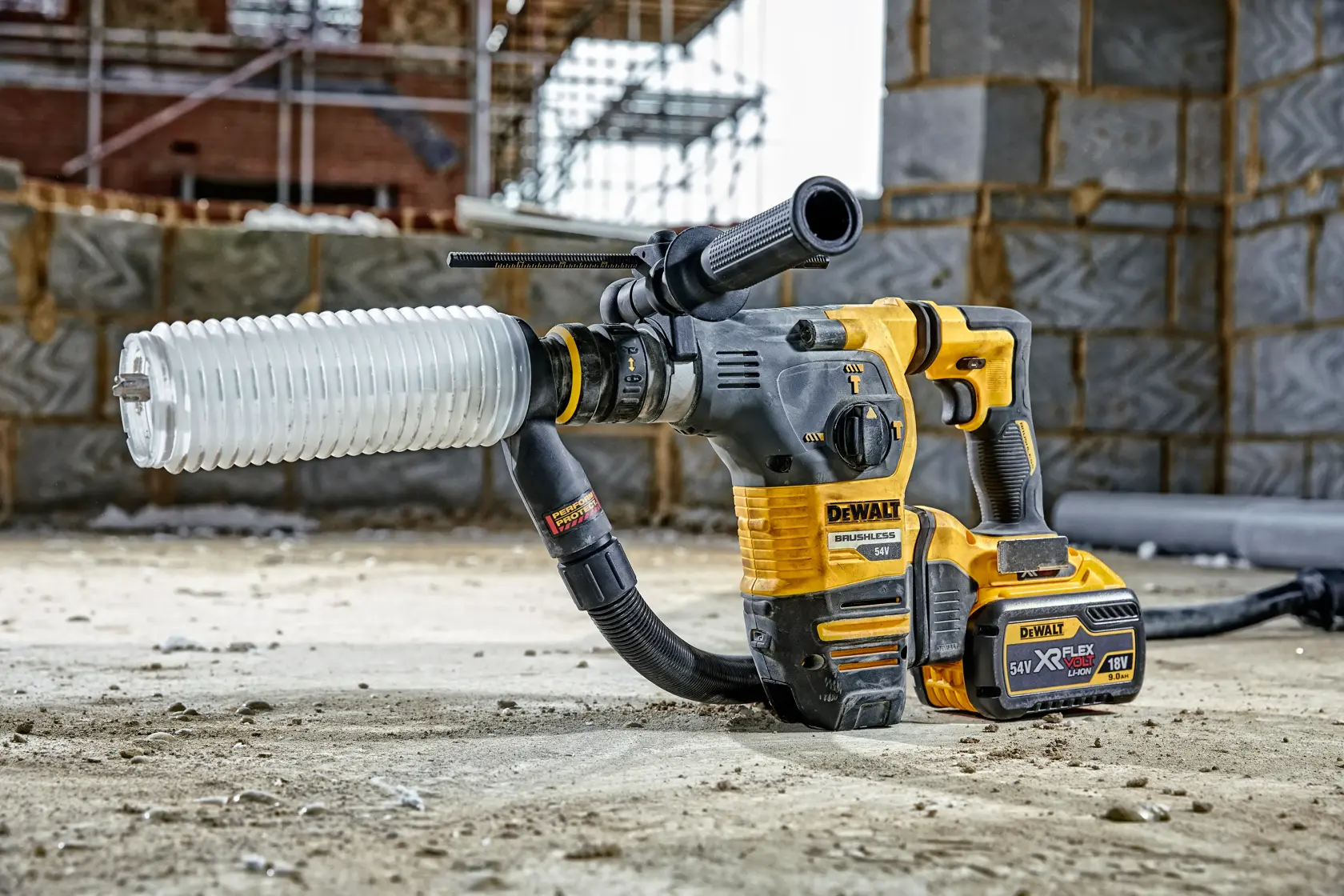 DEWALT cordless hammer drill with dust extractor attachment on a construction site floor with brick wall in background.