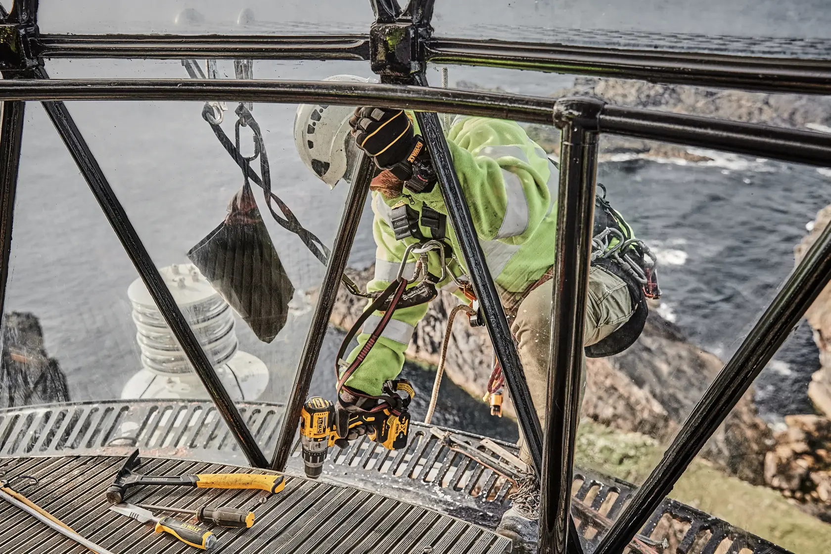 Worker using DEWALT tools inside a lighthouse with a sea view, wearing safety gear and helmet.