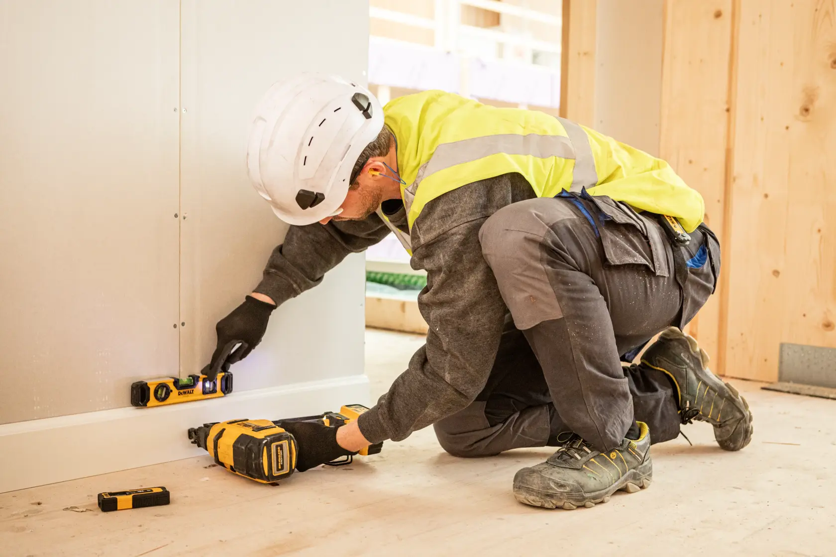 Worker using DEWALT tools and level for wall installation at a construction site.