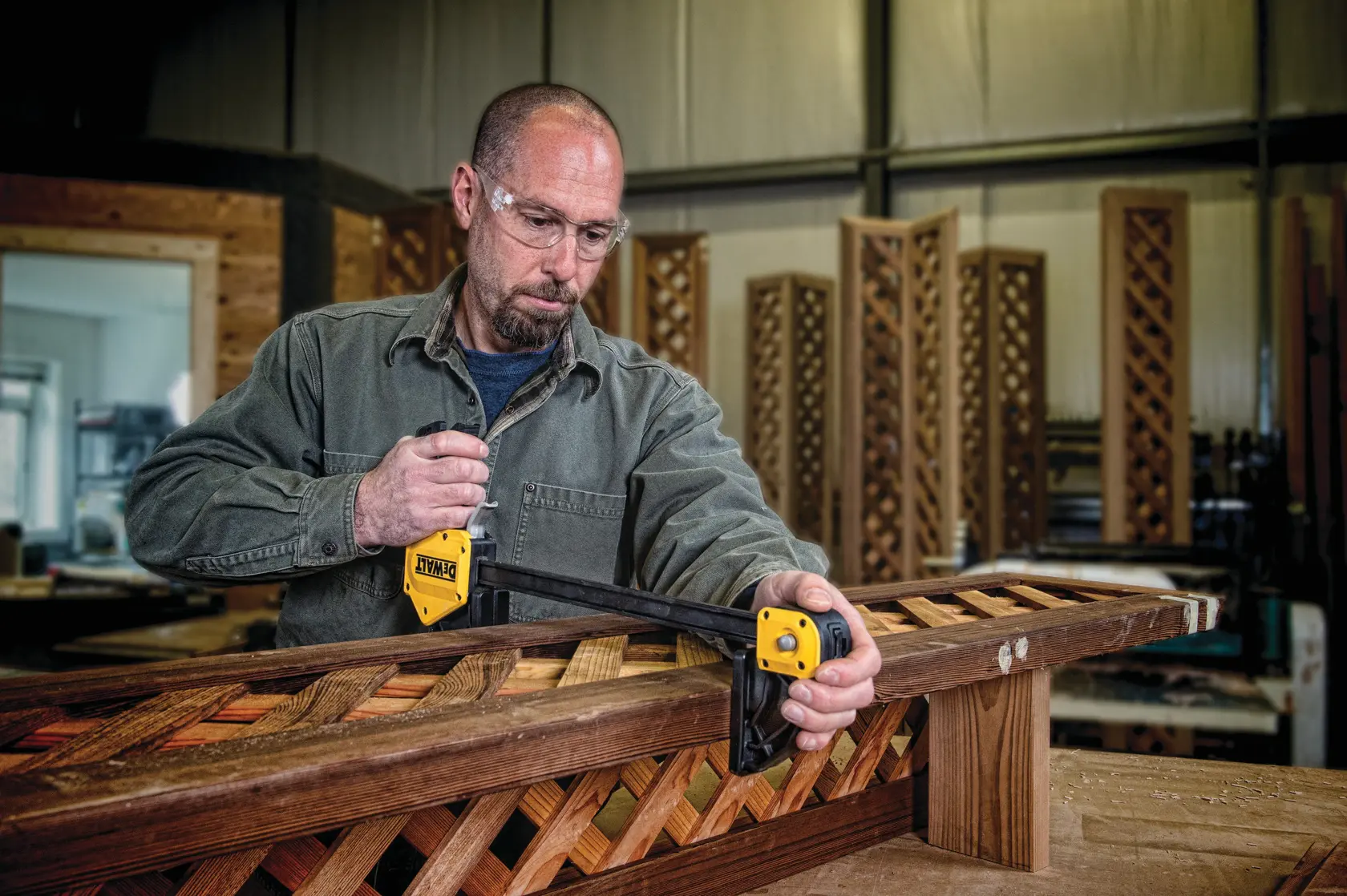 Person uses a DEWALT clamp to secure a wooden frame in a workshop. Face is blurred for privacy.