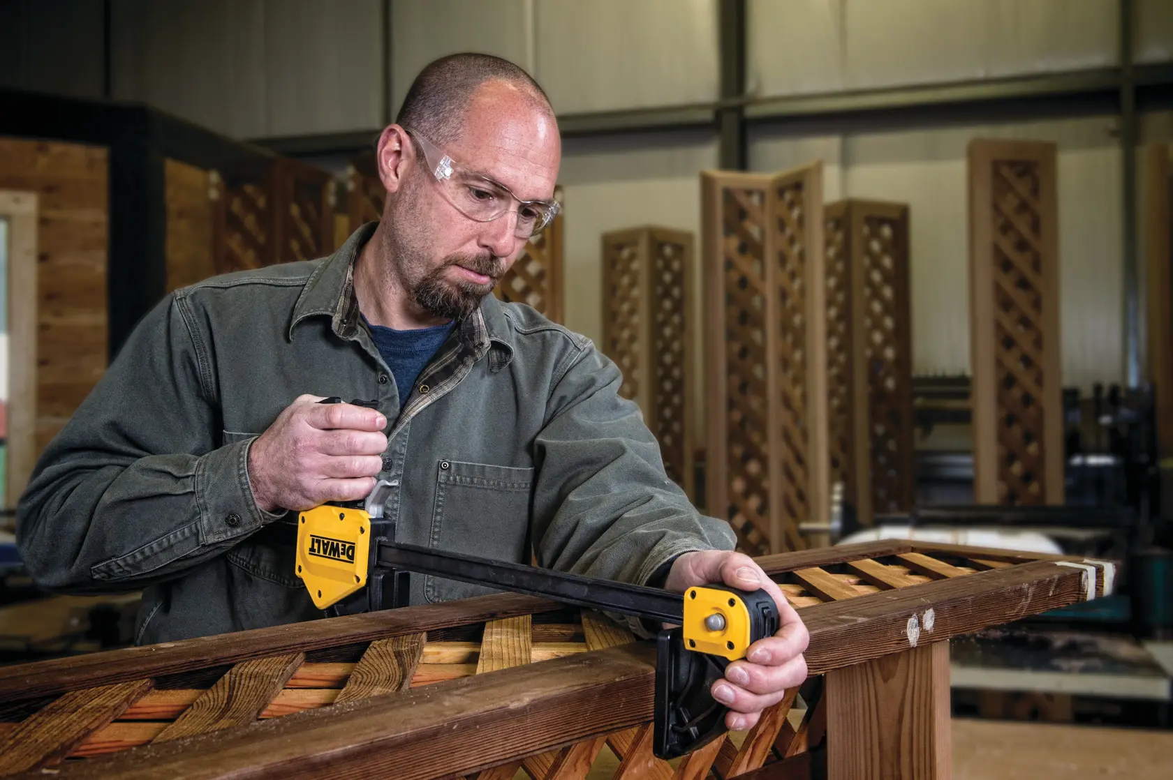 Person using a DEWALT bar clamp to secure wooden boards in a workshop.