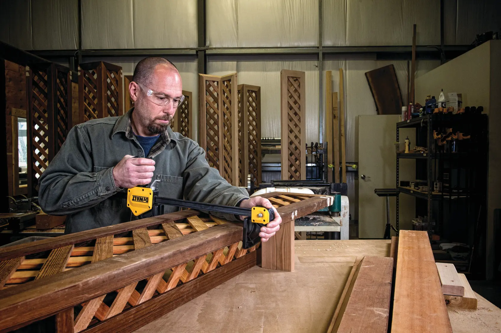 Person using a DEWALT clamp to secure wooden pieces in a workshop setting with lattice woodwork visible.