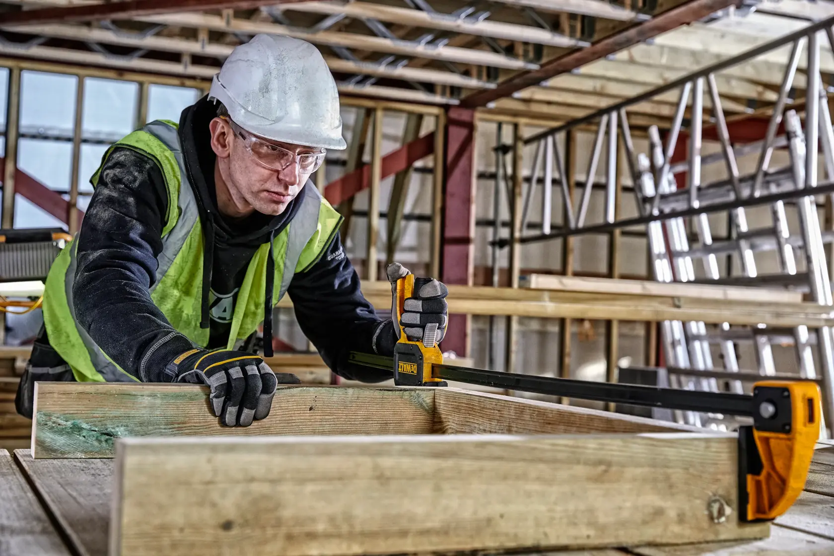 Person using DEWALT bar clamp DWHT0-83187 to secure wooden boards at a construction site.