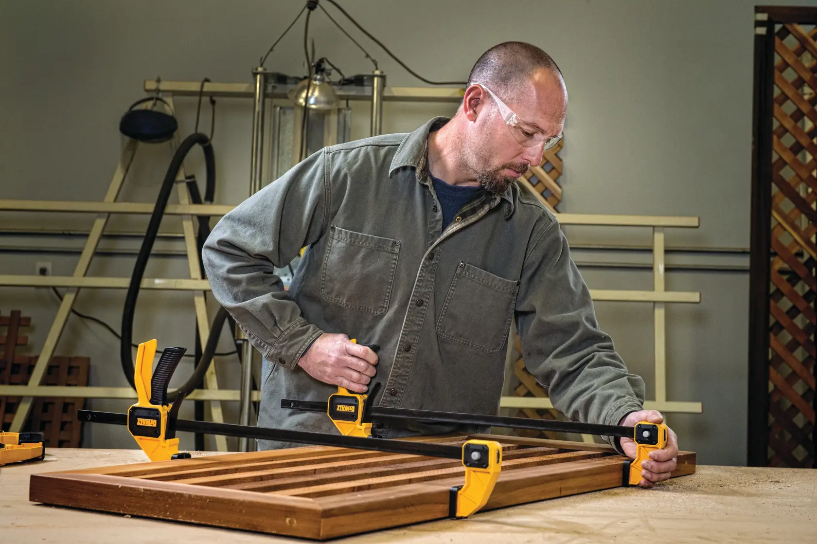Person using DEWALT bar clamps to secure a wooden panel on a workbench in a workshop.