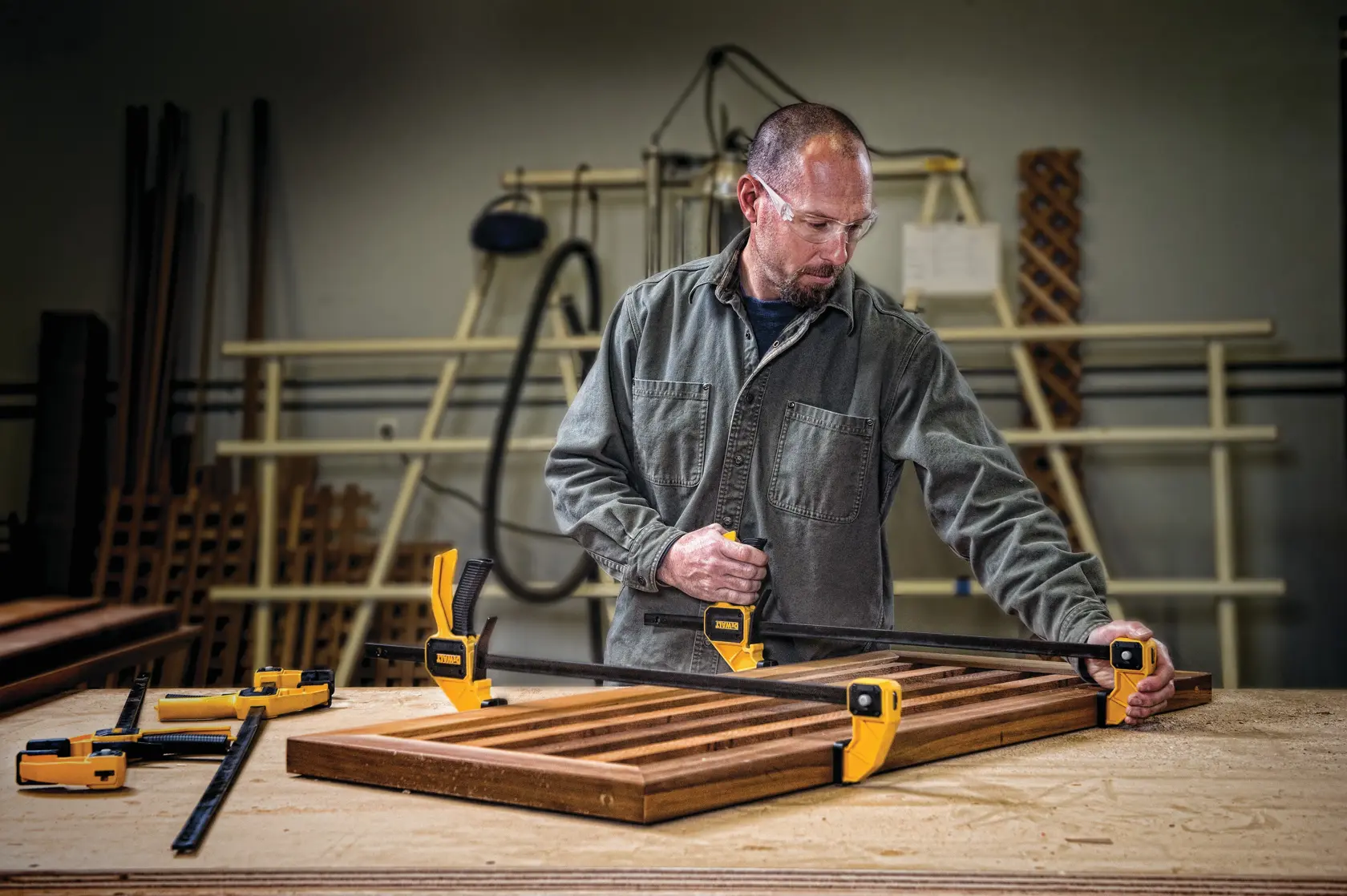 Person uses DEWALT clamps to secure wooden boards on a workbench in a workshop.