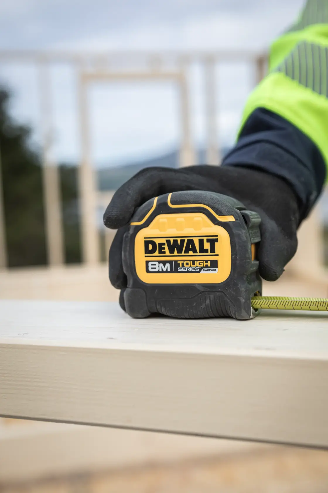 Metro a nastro DEWALT 8M Tough Series tenuto da una mano guantata su una tavola di legno.