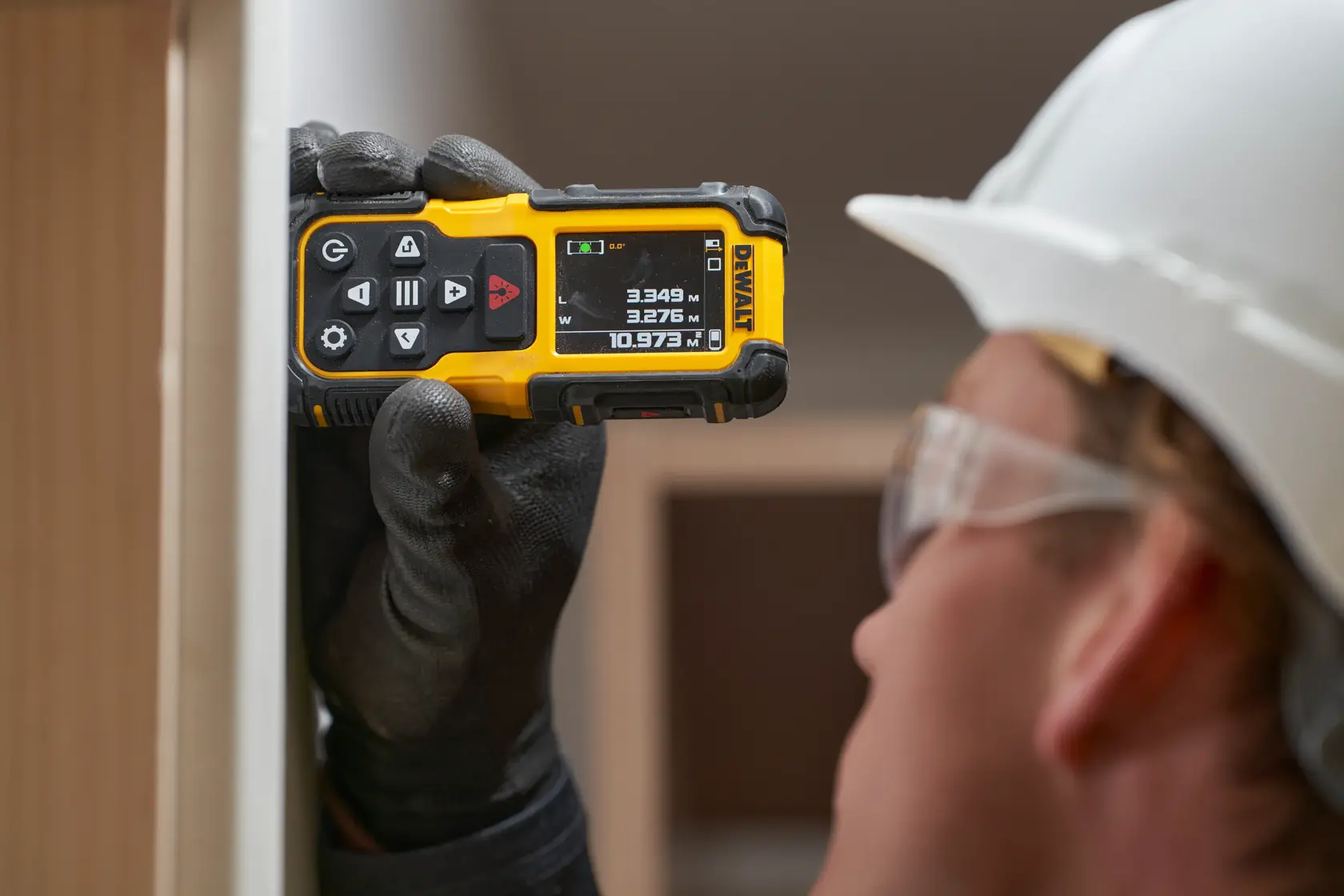 Operaio usa misuratore laser DEWALT su telaio in legno, con casco e giubbotto riflettente.