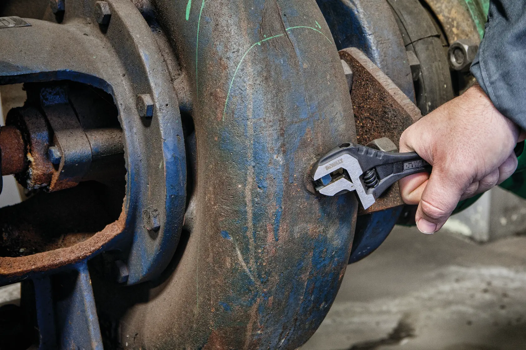 Hand using a DEWALT adjustable wrench to tighten a bolt on a large, industrial metal pipe.