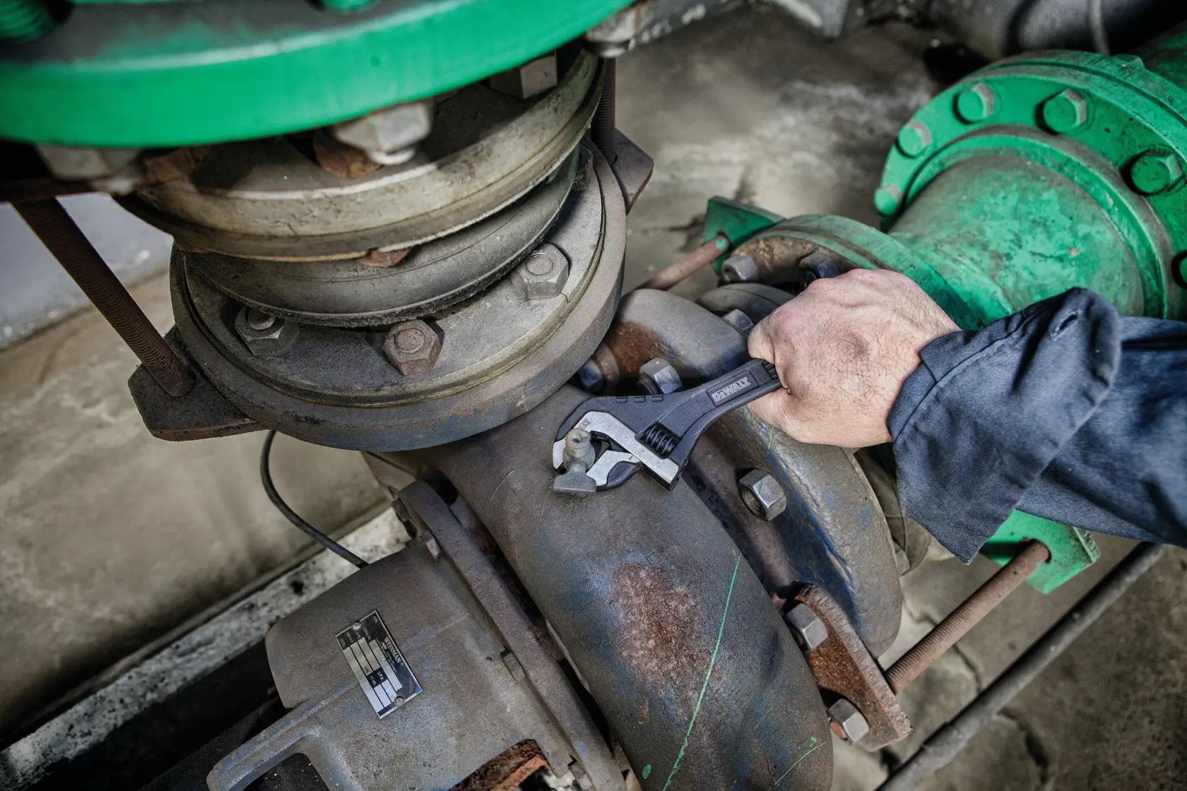 Hand uses DEWALT adjustable wrench on an industrial pipe joint with green fittings.