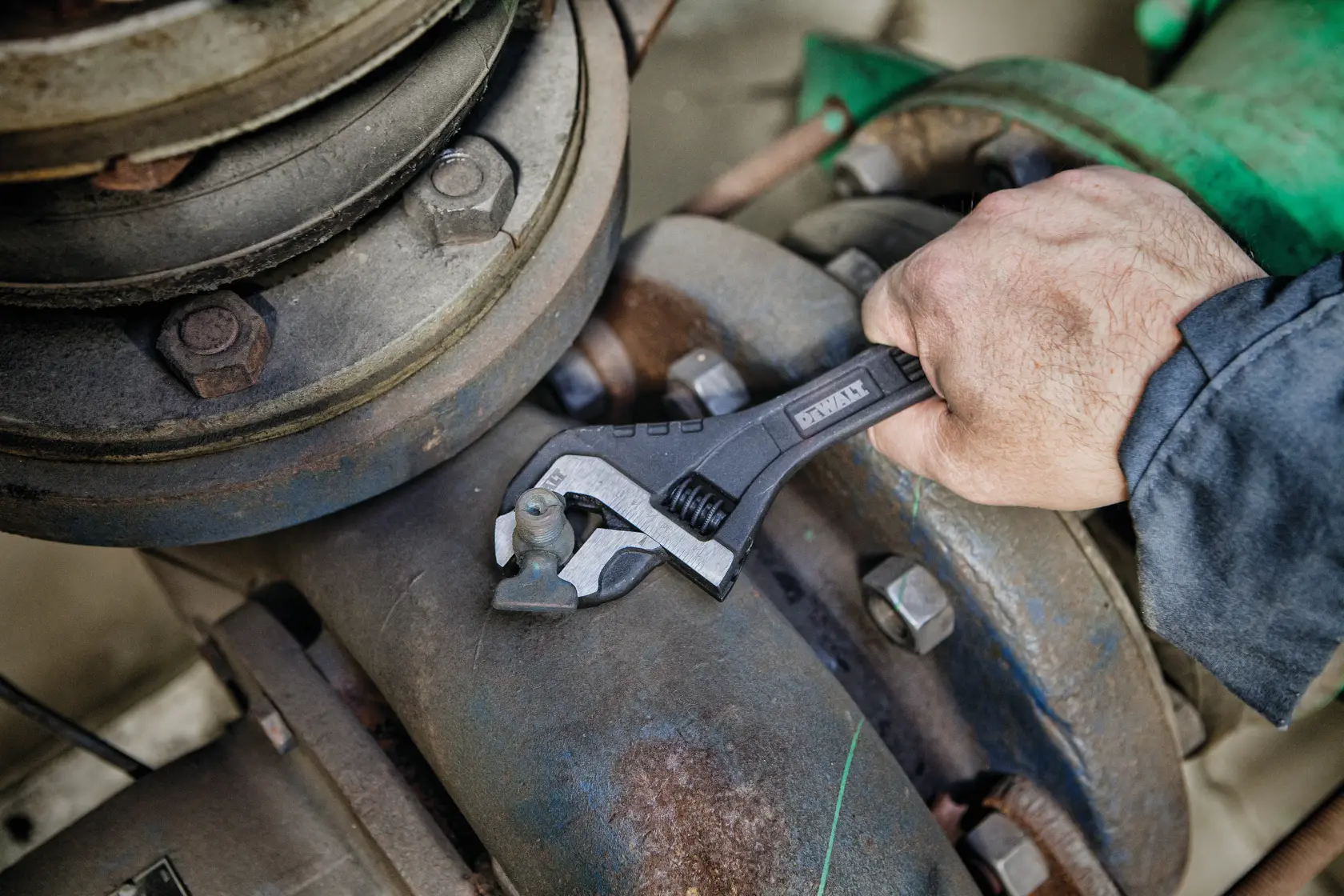 Hand uses DEWALT adjustable wrench on industrial pipe bolt.