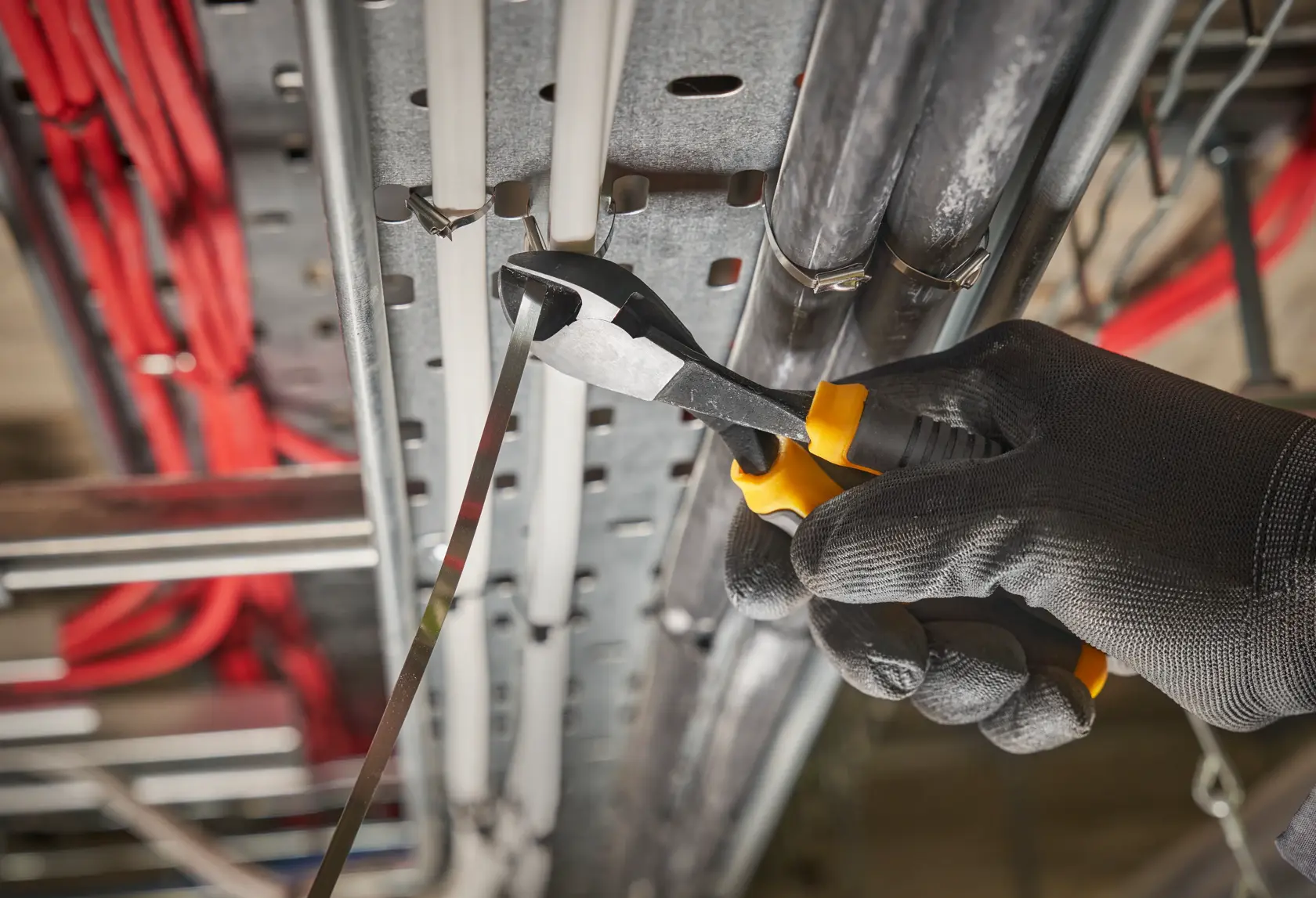 Gloved hand uses DEWALT pliers to cut metal cable tie on electrical installation.
