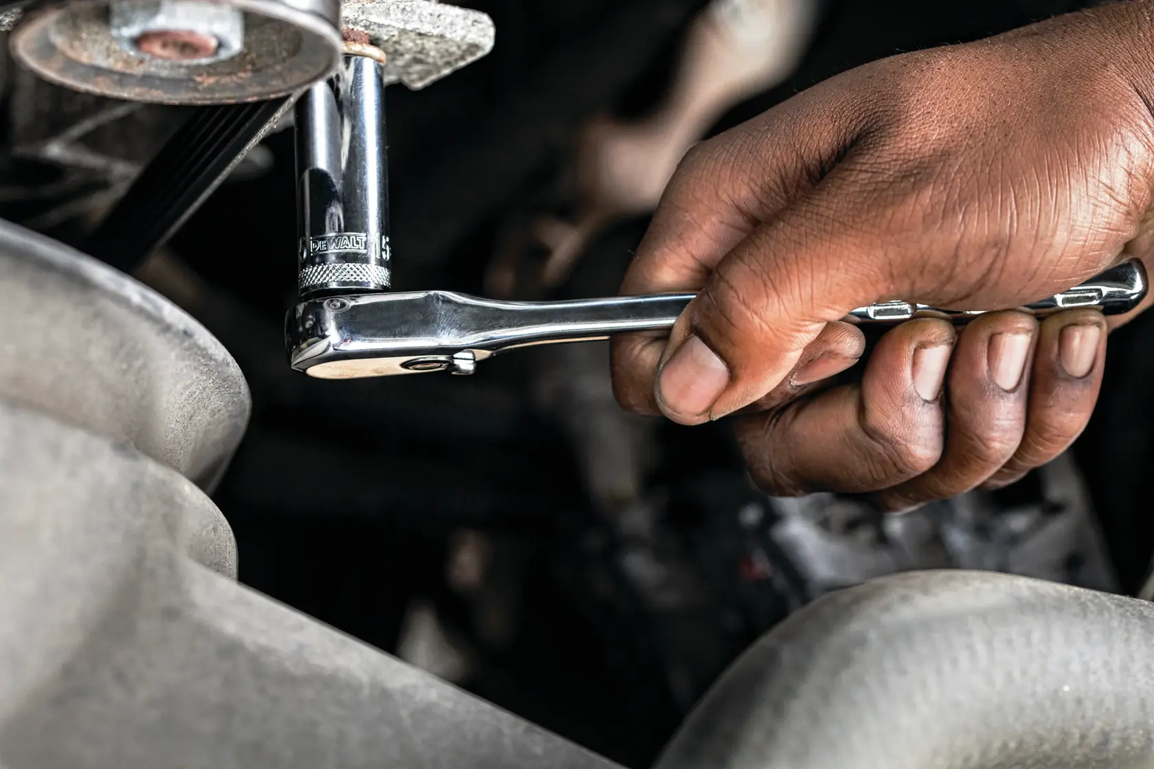 Hand using a DEWALT ratchet wrench to tighten a fastener in an engine compartment.