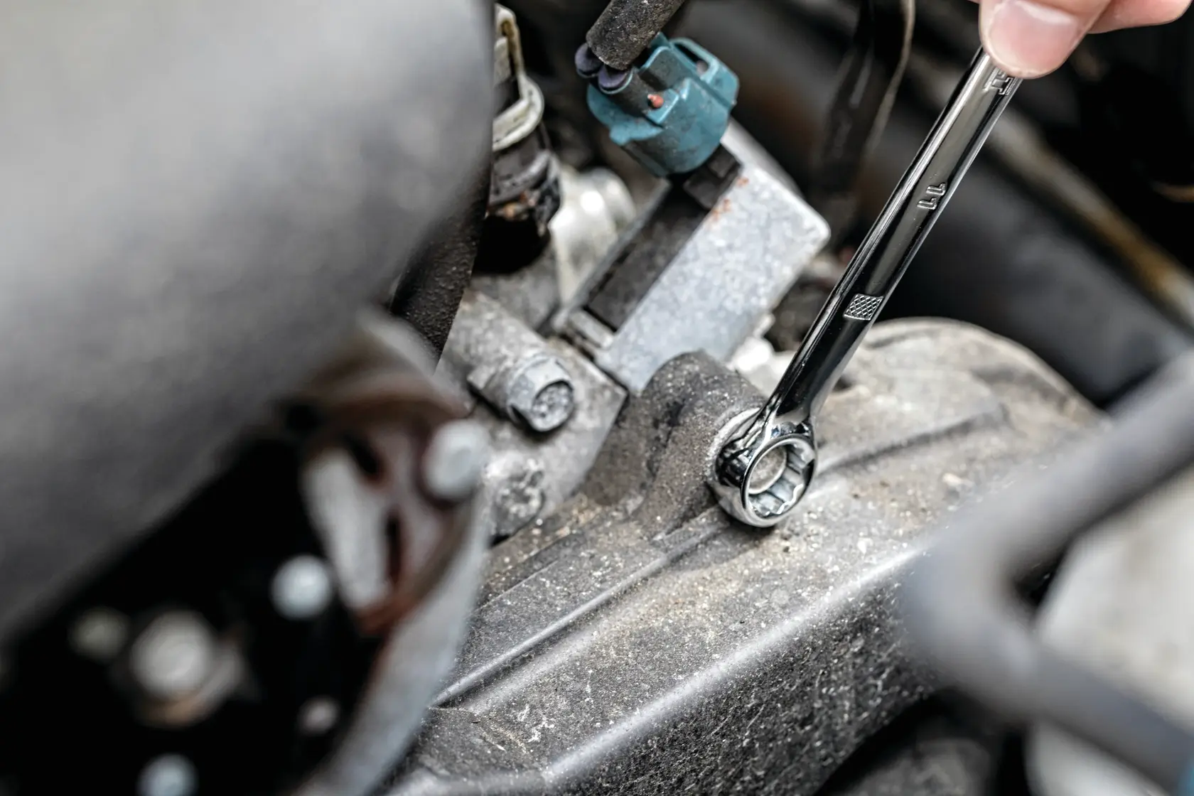 A hand uses a DEWALT ratcheting wrench to tighten a bolt on a dusty engine part.