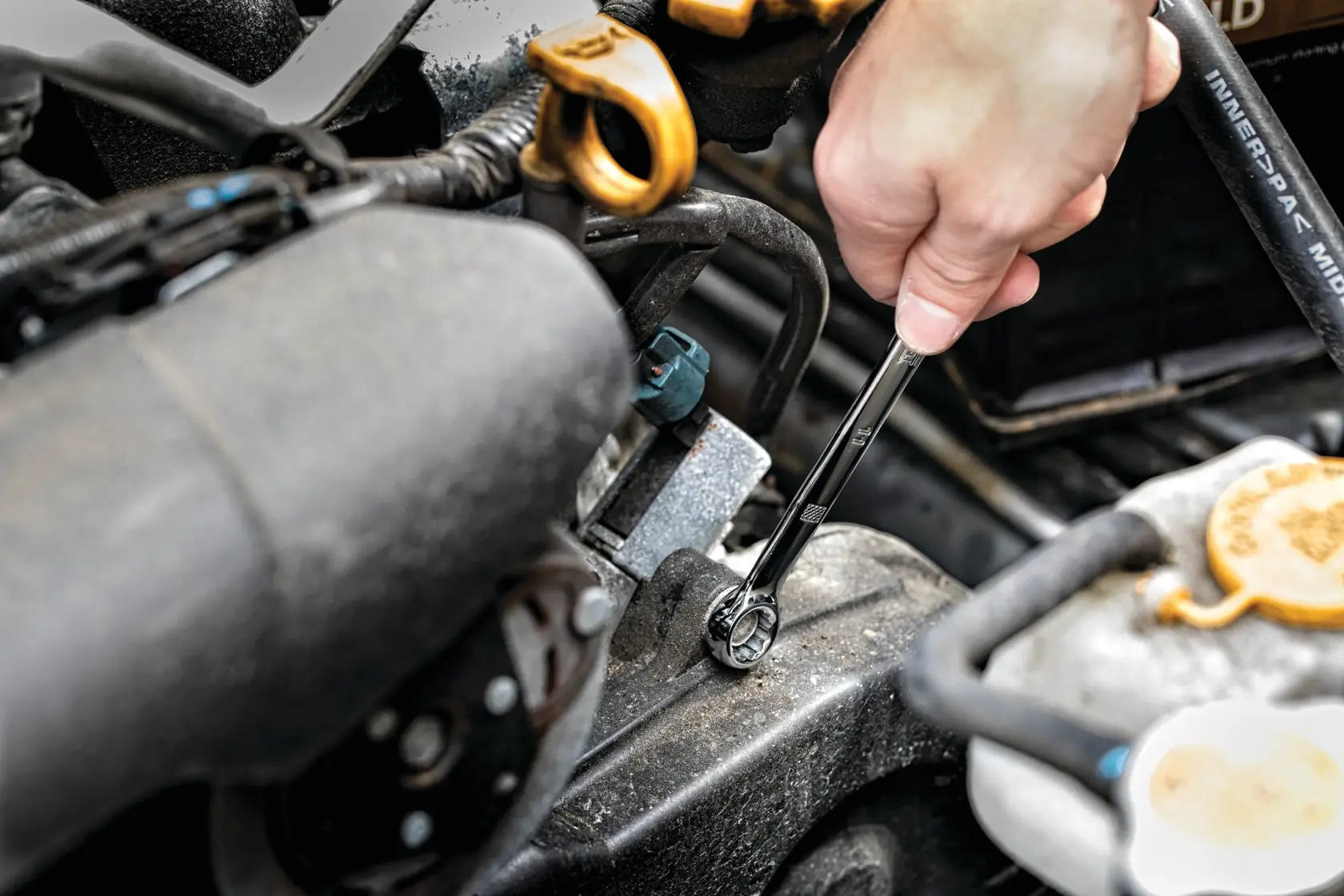 Hand uses DEWALT wrench to tighten bolt in car engine compartment.