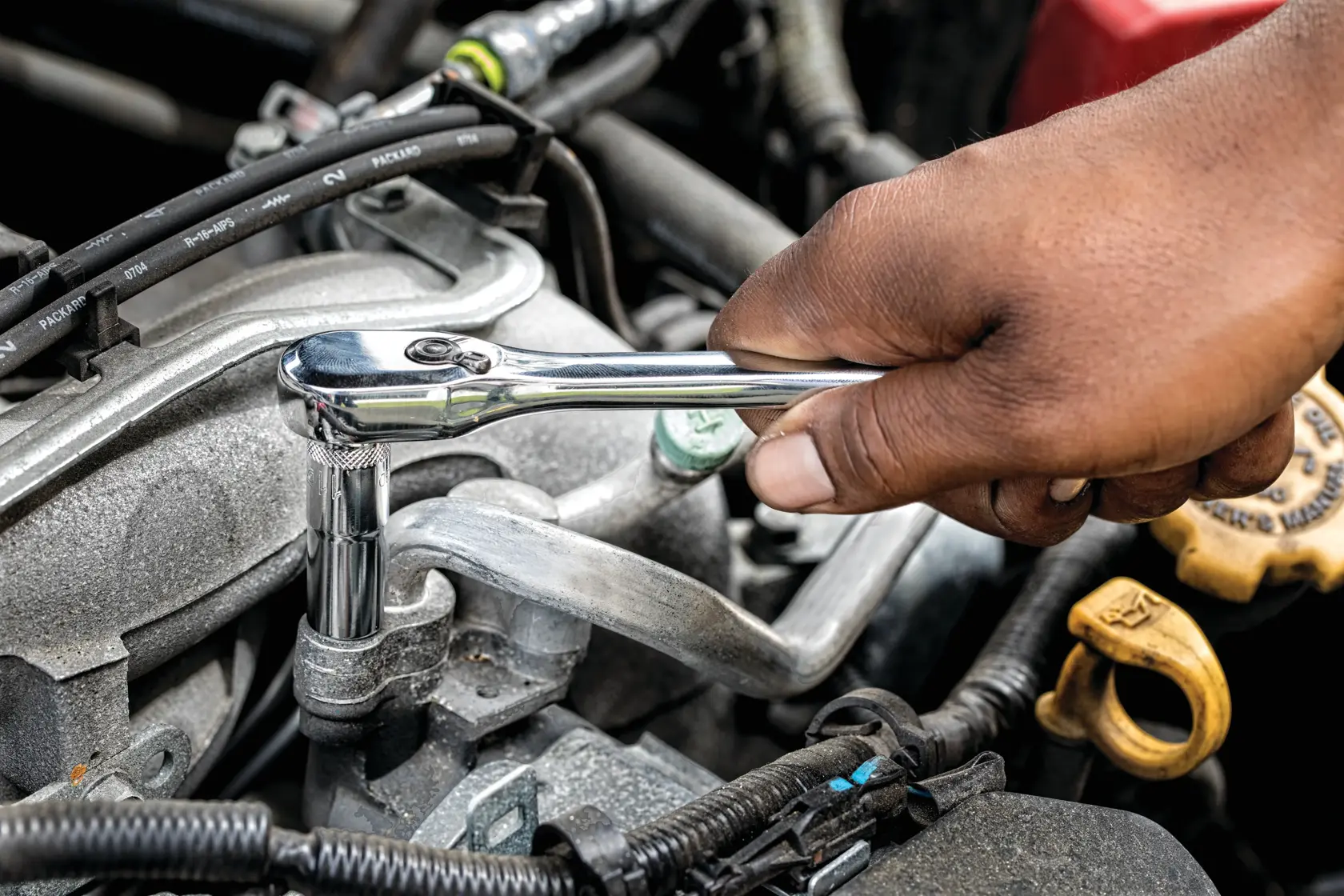 Hand using a DEWALT ratchet wrench on a bolt inside a car engine compartment.