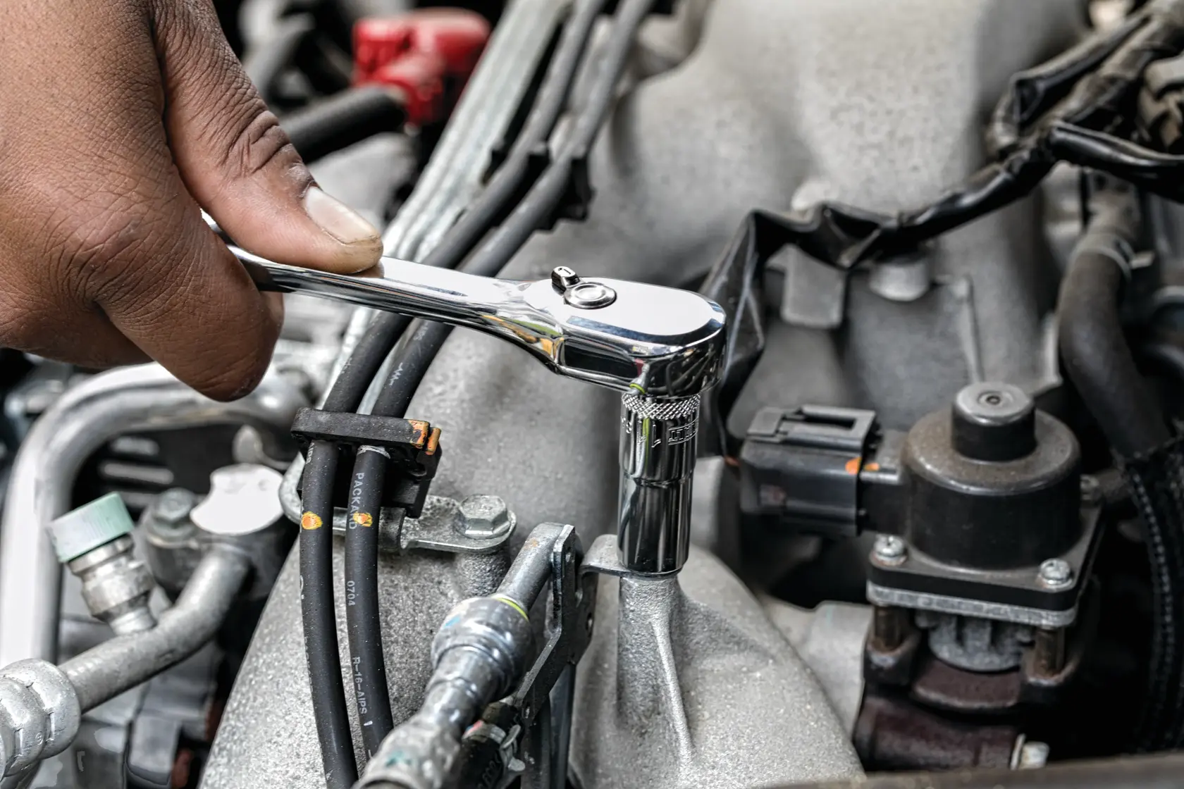 Hand using a DEWALT ratchet on a bolt in a car engine compartment.