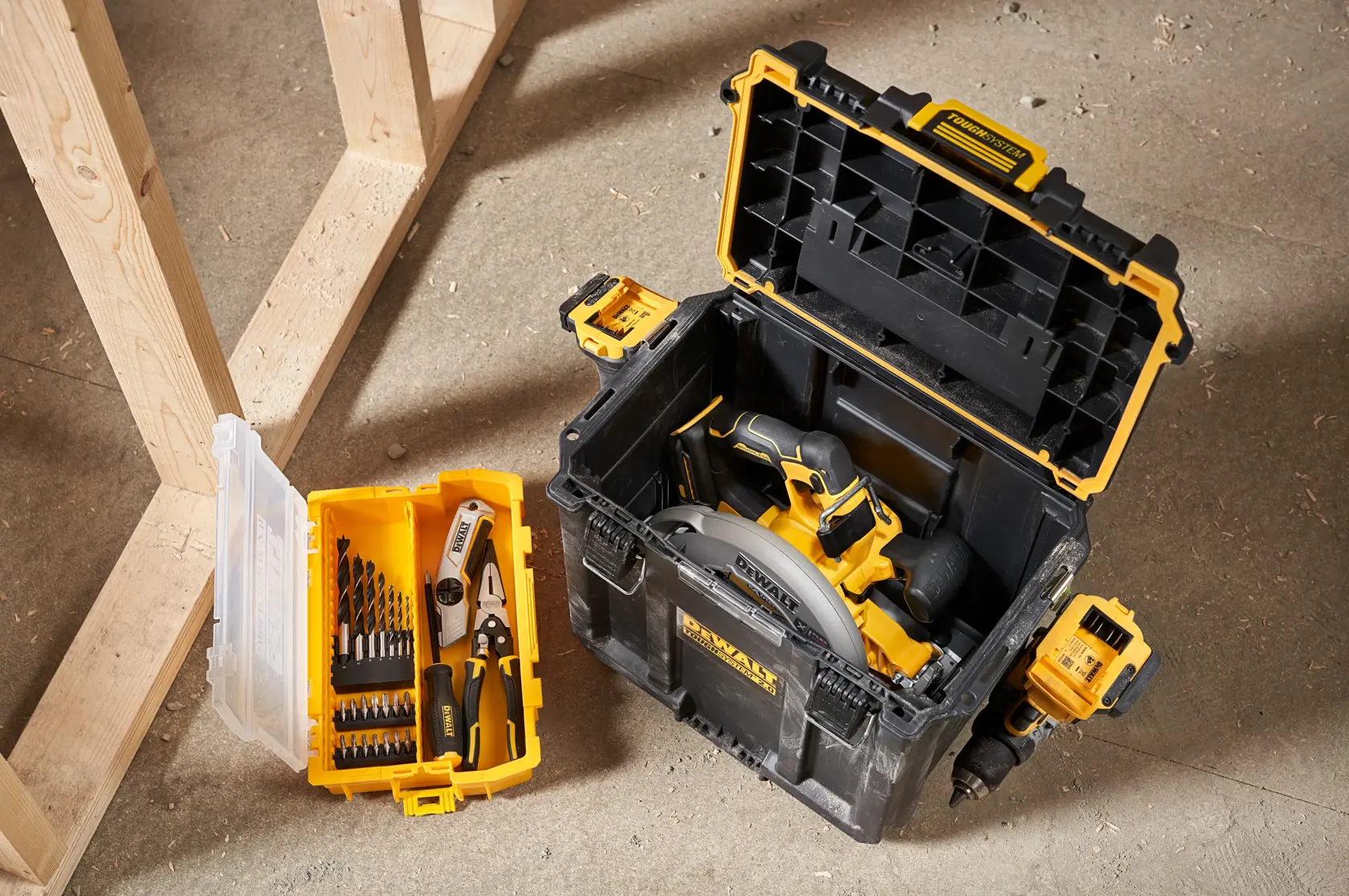 En DEWALT verktøykasse med lokket åpnet, som inneholder en sirkelsag. Ved siden av står en mindre gul og transparent organizer med borer og tang, begge plassert på verkstedgulvet.