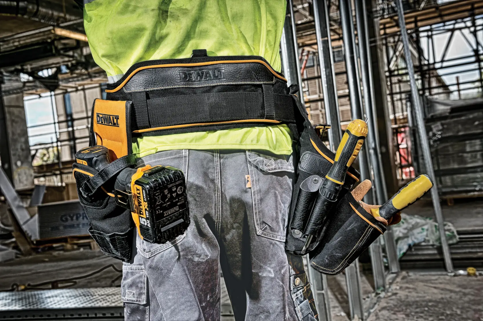 Worker wearing DEWALT tool belt with various tools at a construction site.