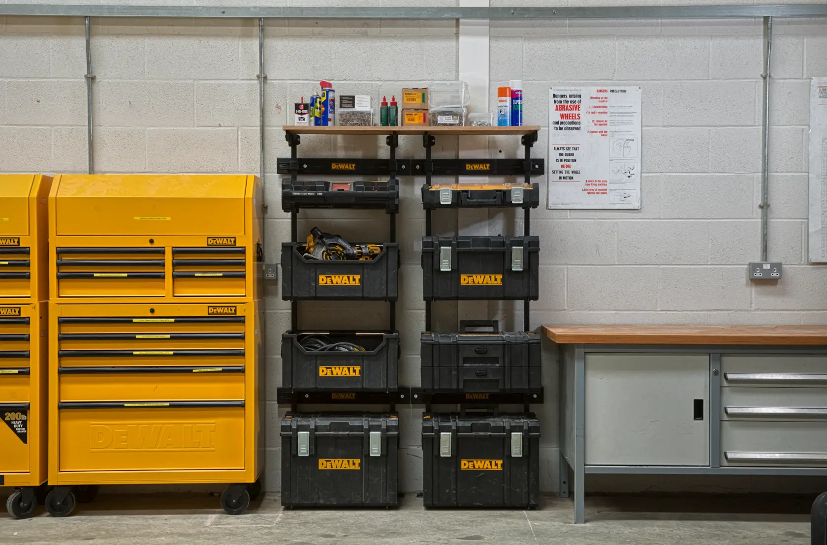 DEWALT toolboxes and storage units organized in a workshop next to a workbench and yellow tool cabinets.
