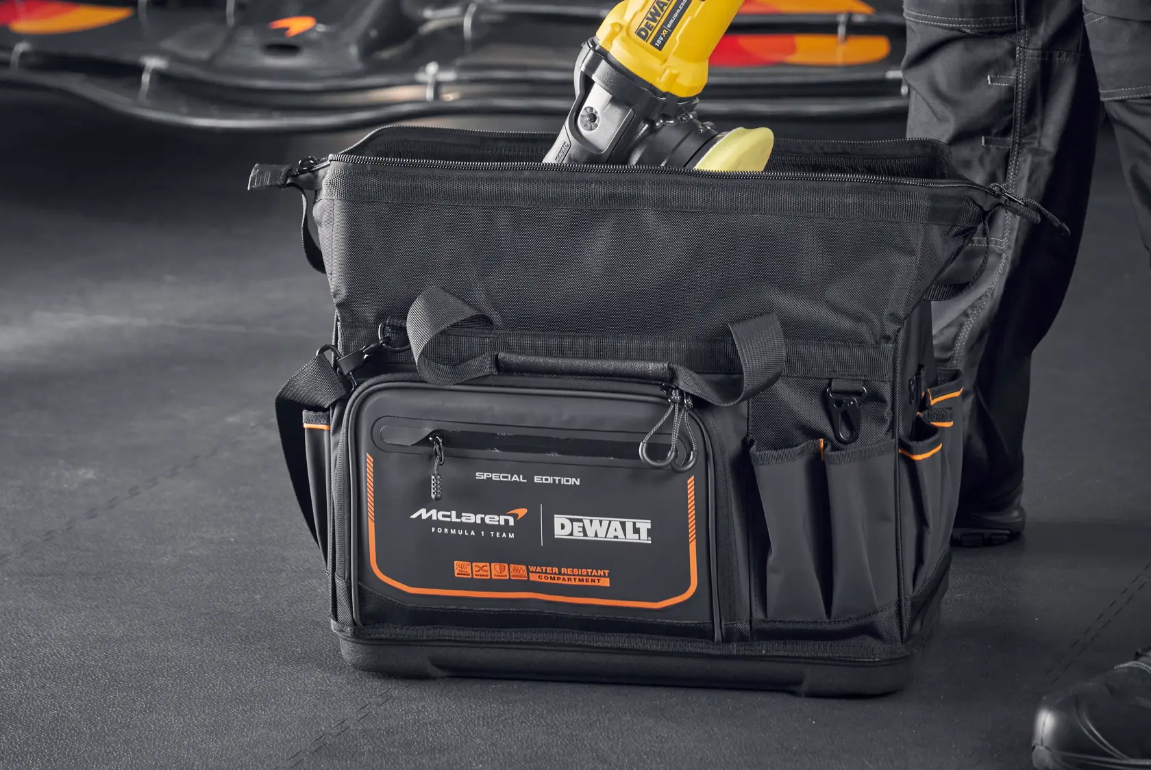 DEWALT McLaren tool bag with multiple compartments, black with orange accents, shown in a workshop setting.