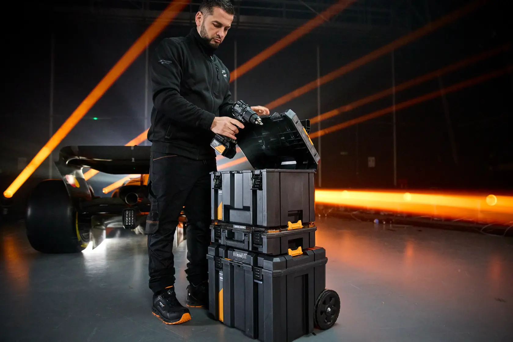 Person using a DEWALT tool storage stack with wheels in an industrial setting, near an illuminated sports car.