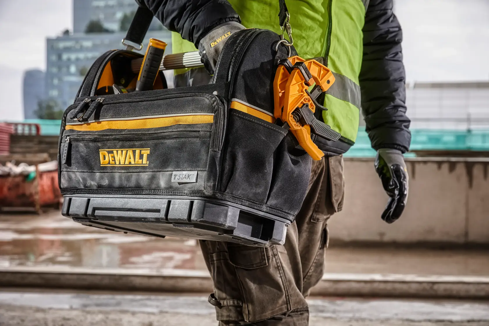 DEWALT tool bag with tools, carried by a worker in outdoor construction setting.