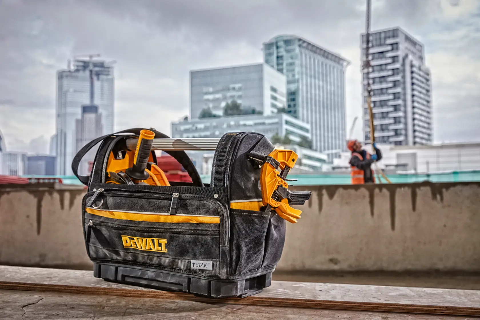 DEWALT tool bag with tools on a construction site, city buildings in background.