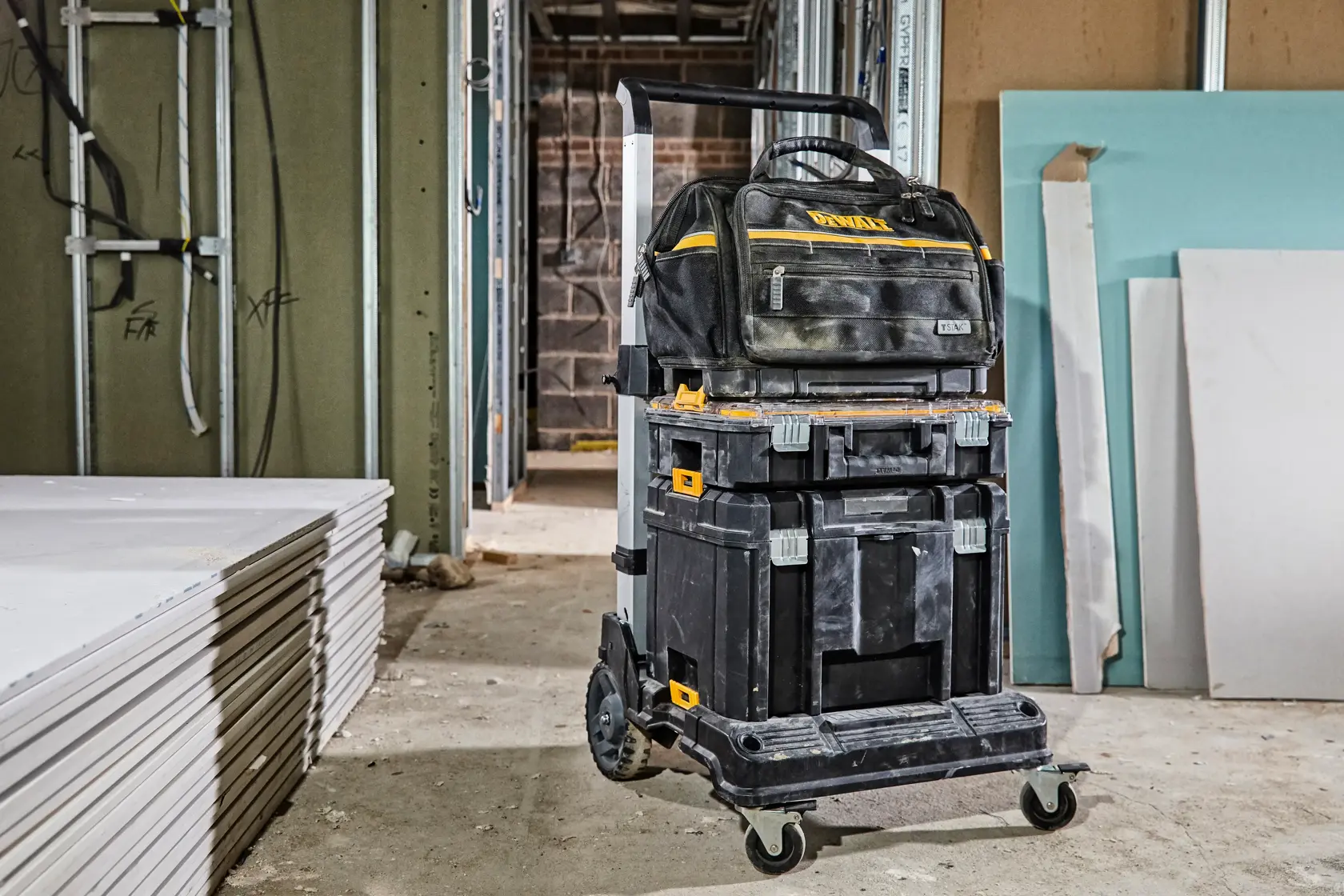 DEWALT tool trolley with stacked toolboxes and bag in a construction site with drywall sheets on the floor.