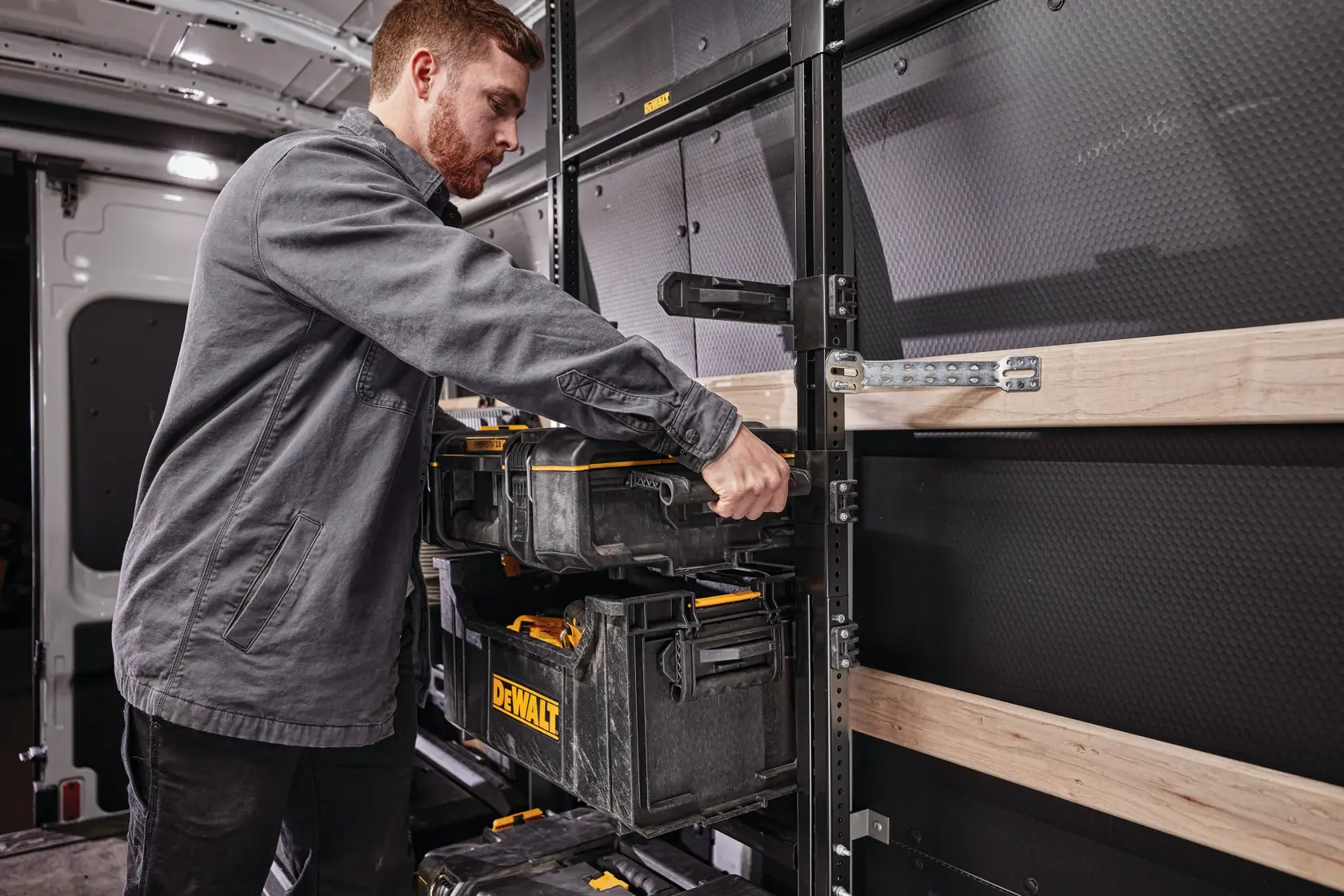 Persona organiza cajas de herramientas DEWALT en estanterías dentro de una furgoneta de trabajo.