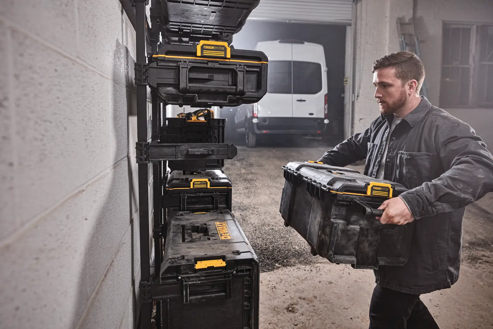 Person stores a DEWALT tool box on a wall rack in a garage with stacked black and yellow tool boxes visible.