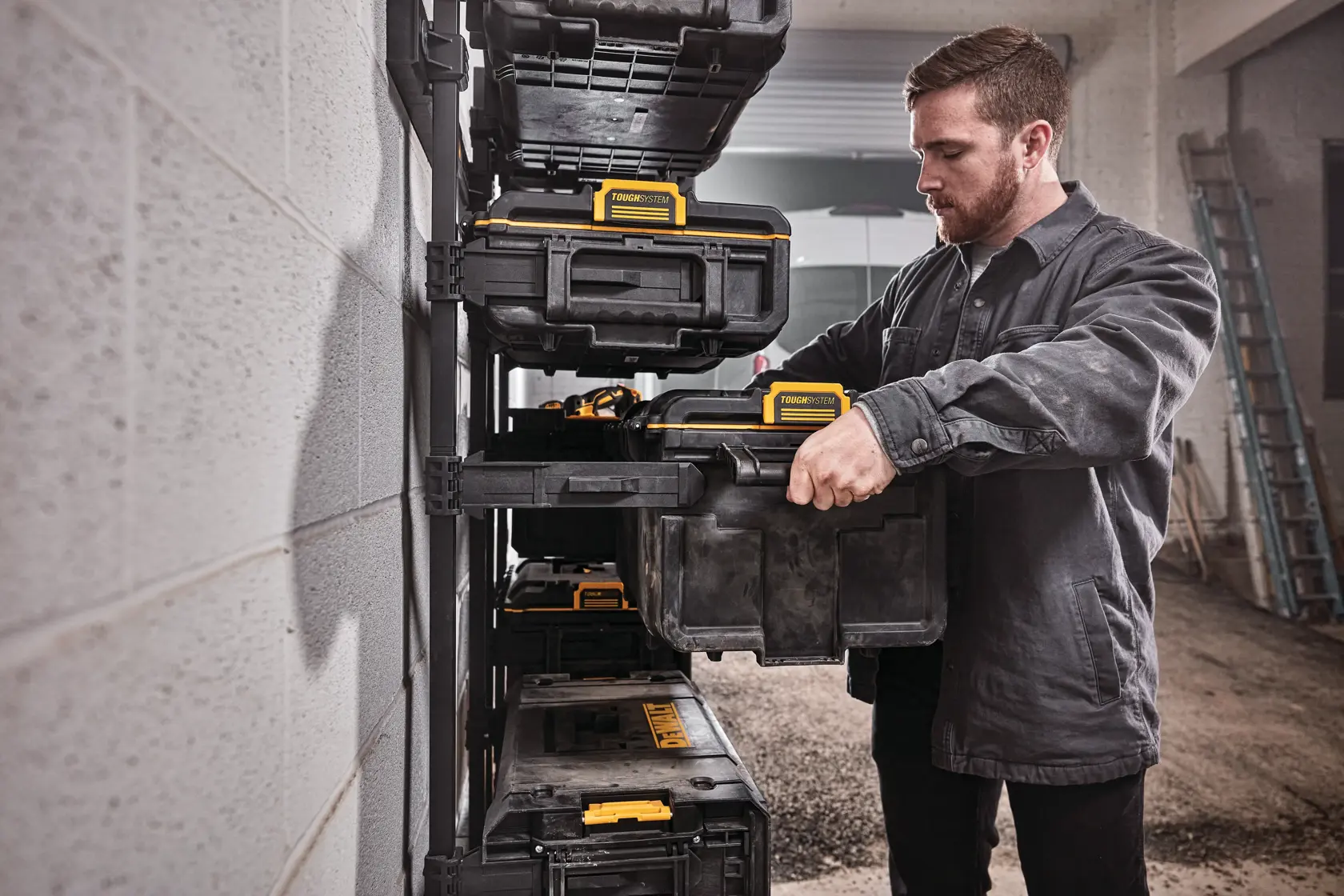 Person places a DEWALT tool box onto a storage rack in a workshop. Several black and yellow tool boxes are visible.