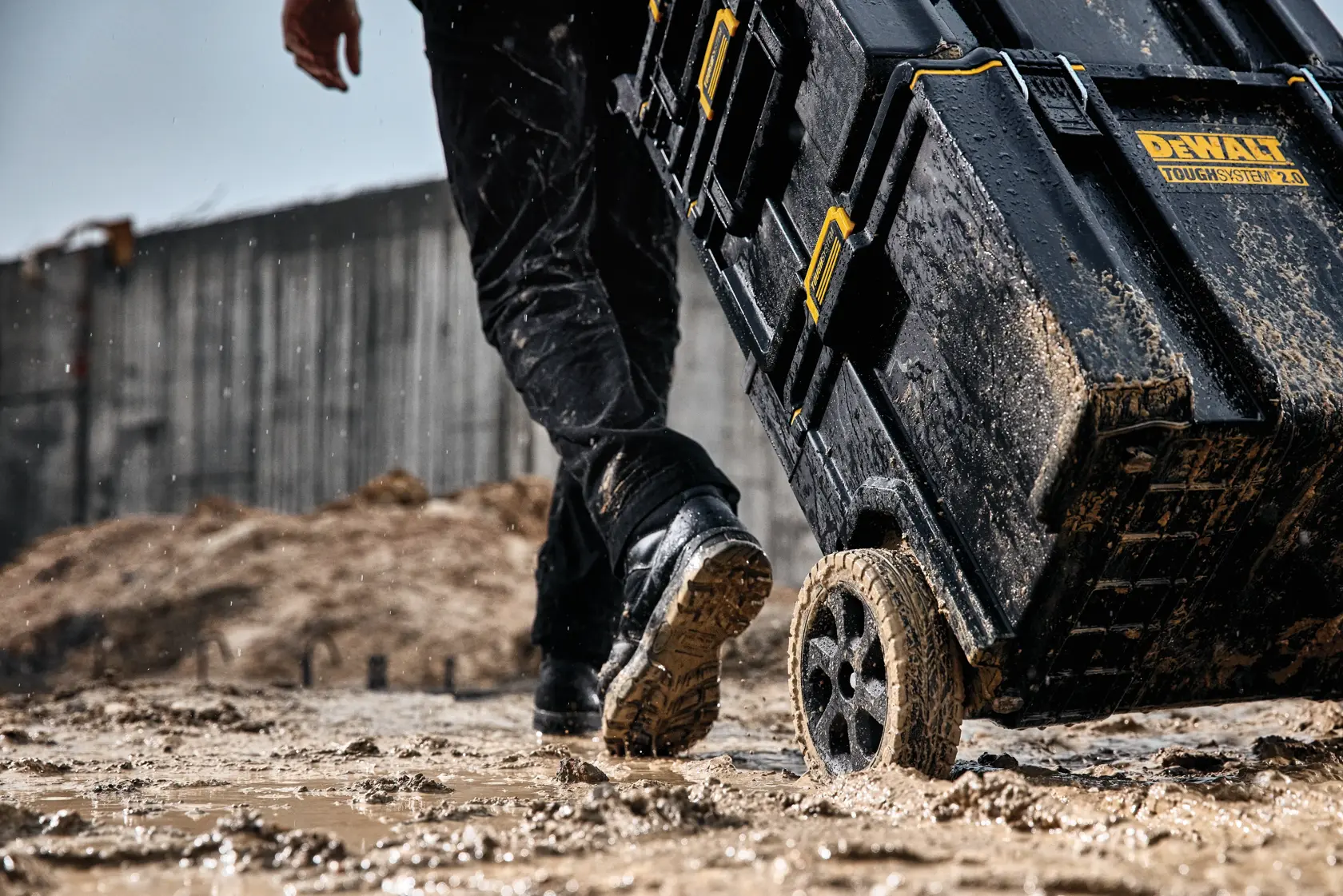 Muddy DEWALT ToughSystem 2.0 toolbox on wheels being pulled across a wet, muddy construction site.