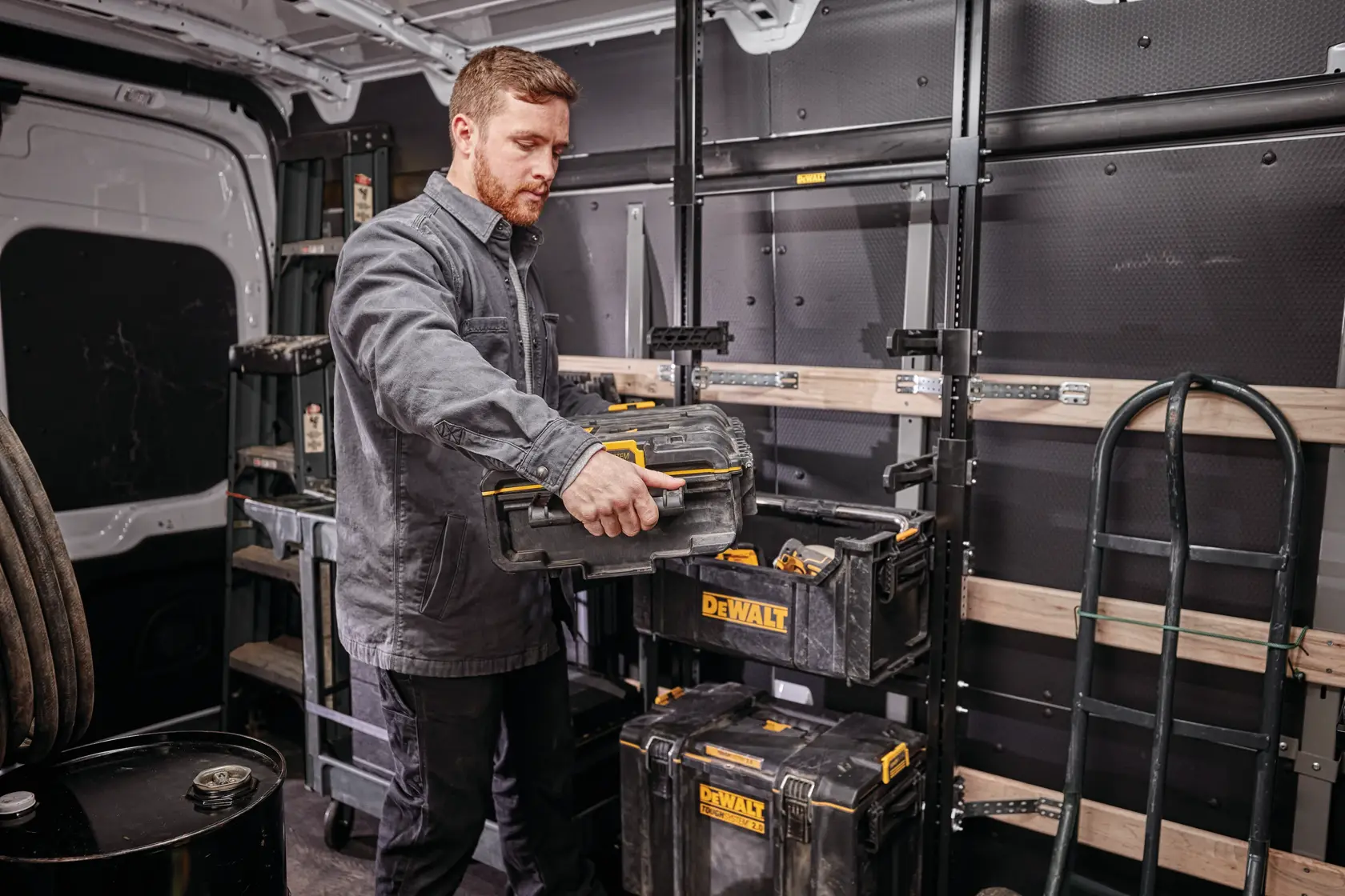Person organizing DEWALT toolboxes inside a work van with shelves and equipment visible in the background.