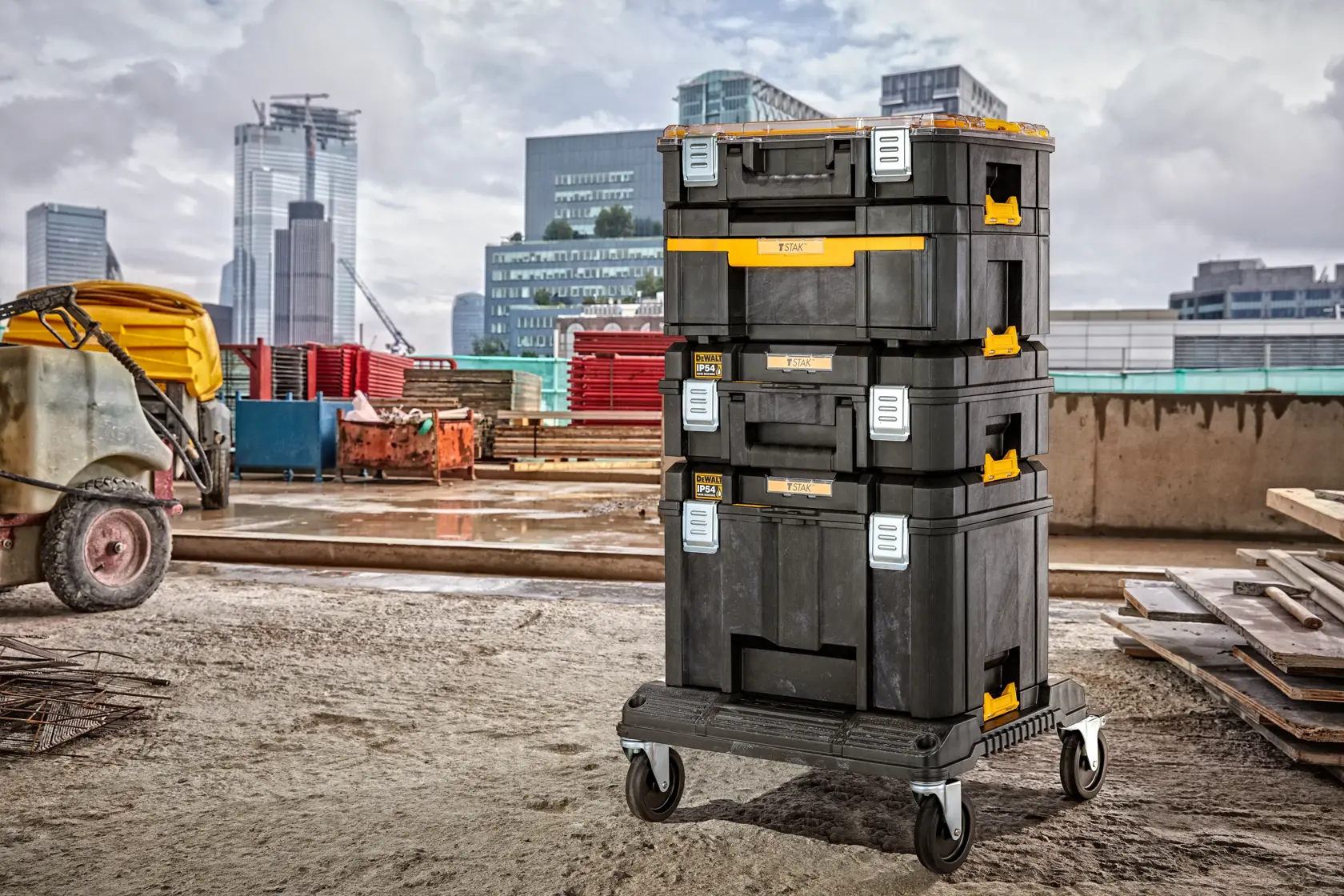 Stacked DEWALT toolboxes on a wheeled base at a construction site with buildings in the background.