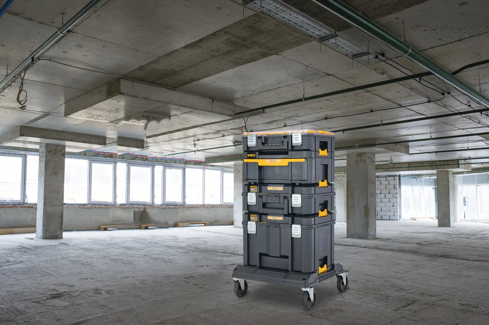 Stacked DEWALT toolboxes on a wheeled cart in an unfinished building with concrete floors and ceiling.