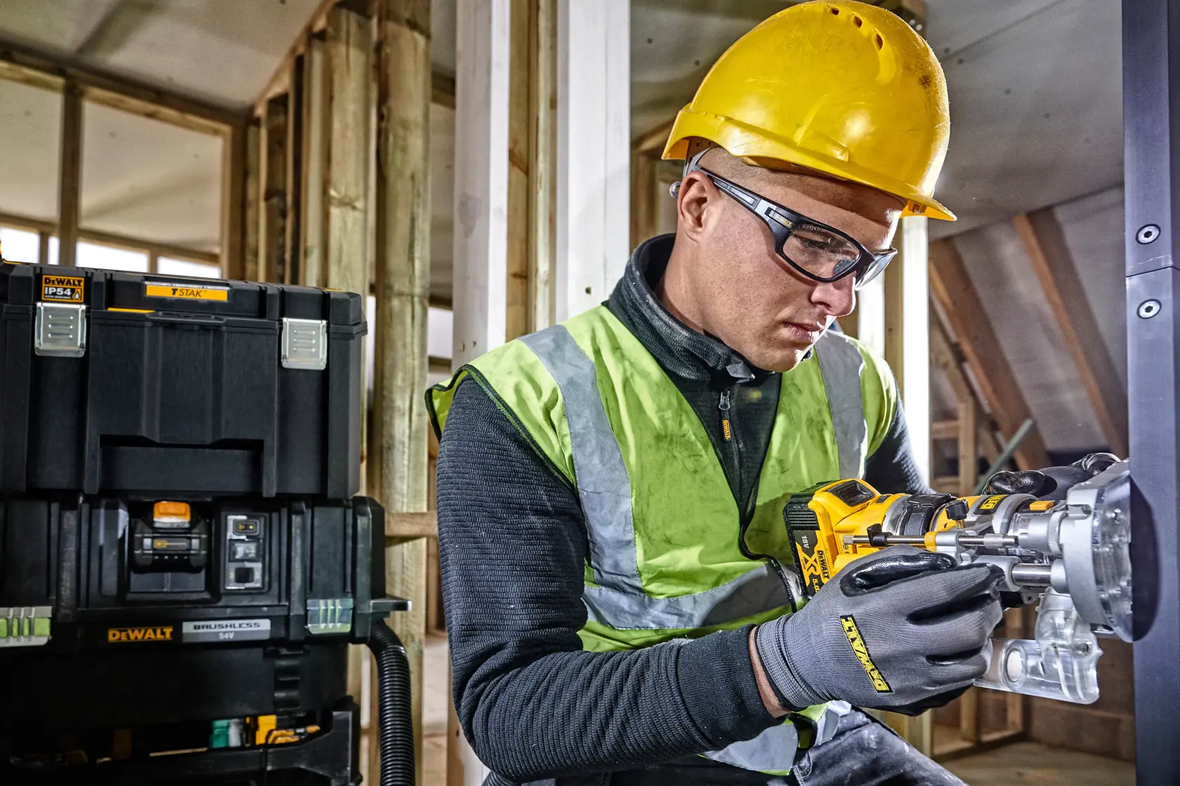 Worker with hard hat and gloves uses DEWALT tool, DEWALT storage box in background at building site.