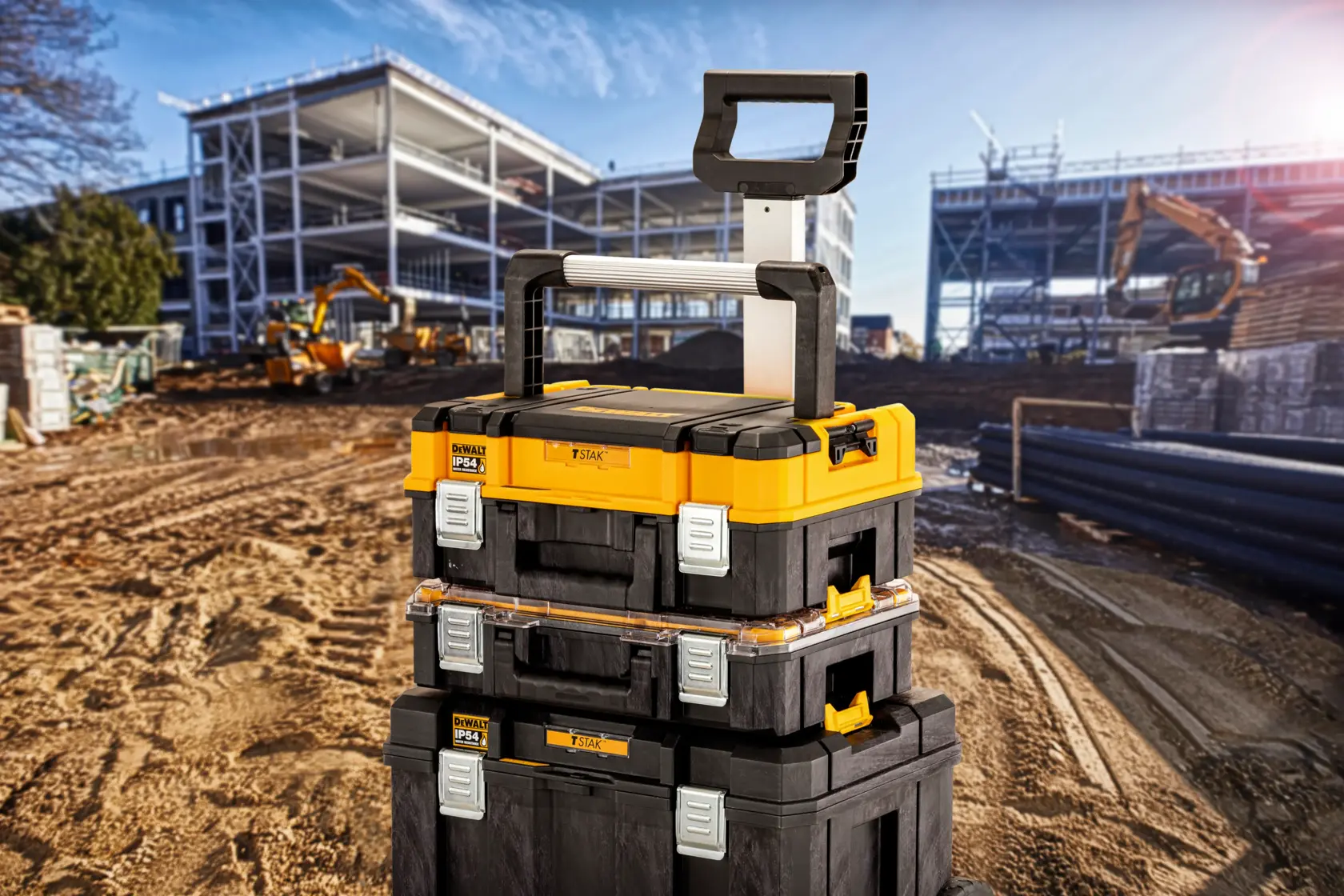 Stacked DEWALT toolboxes with handle on a construction site, metal frames and machinery visible in background.