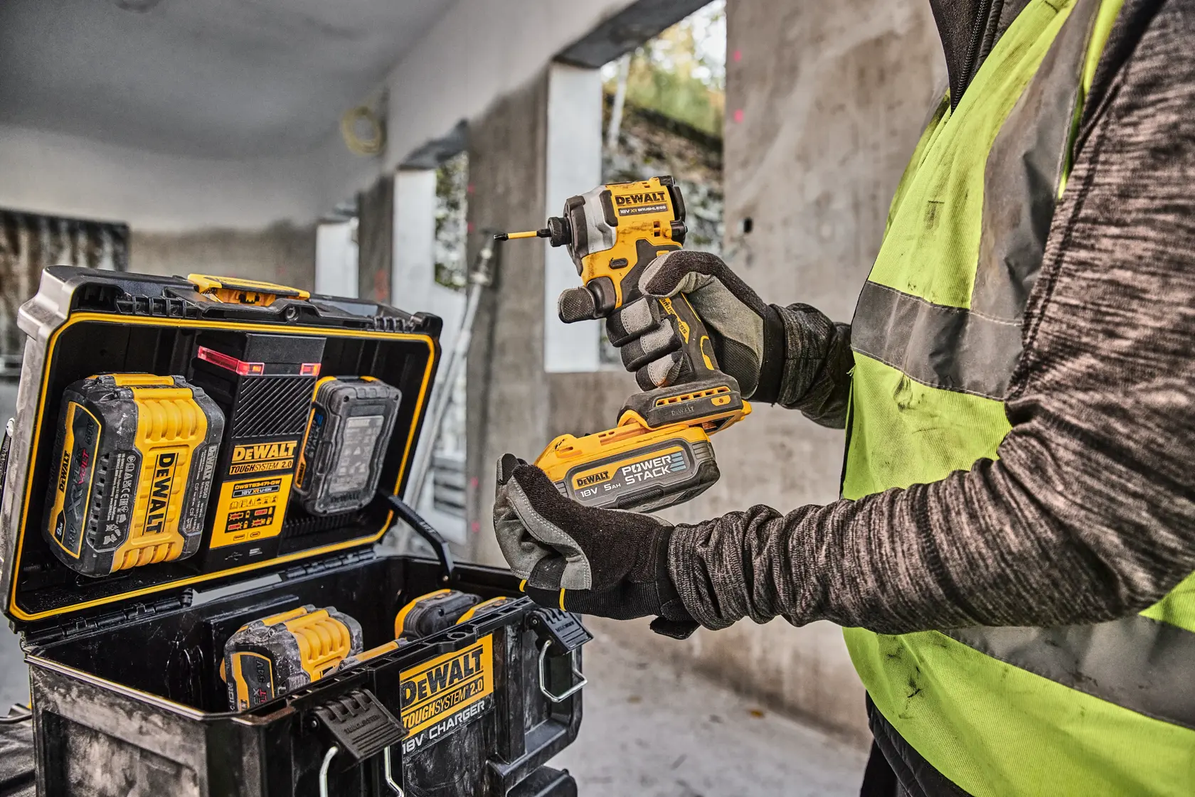 Persona con utensile DEWALT e batteria, valigetta e batterie DEWALT visibili in cantiere.