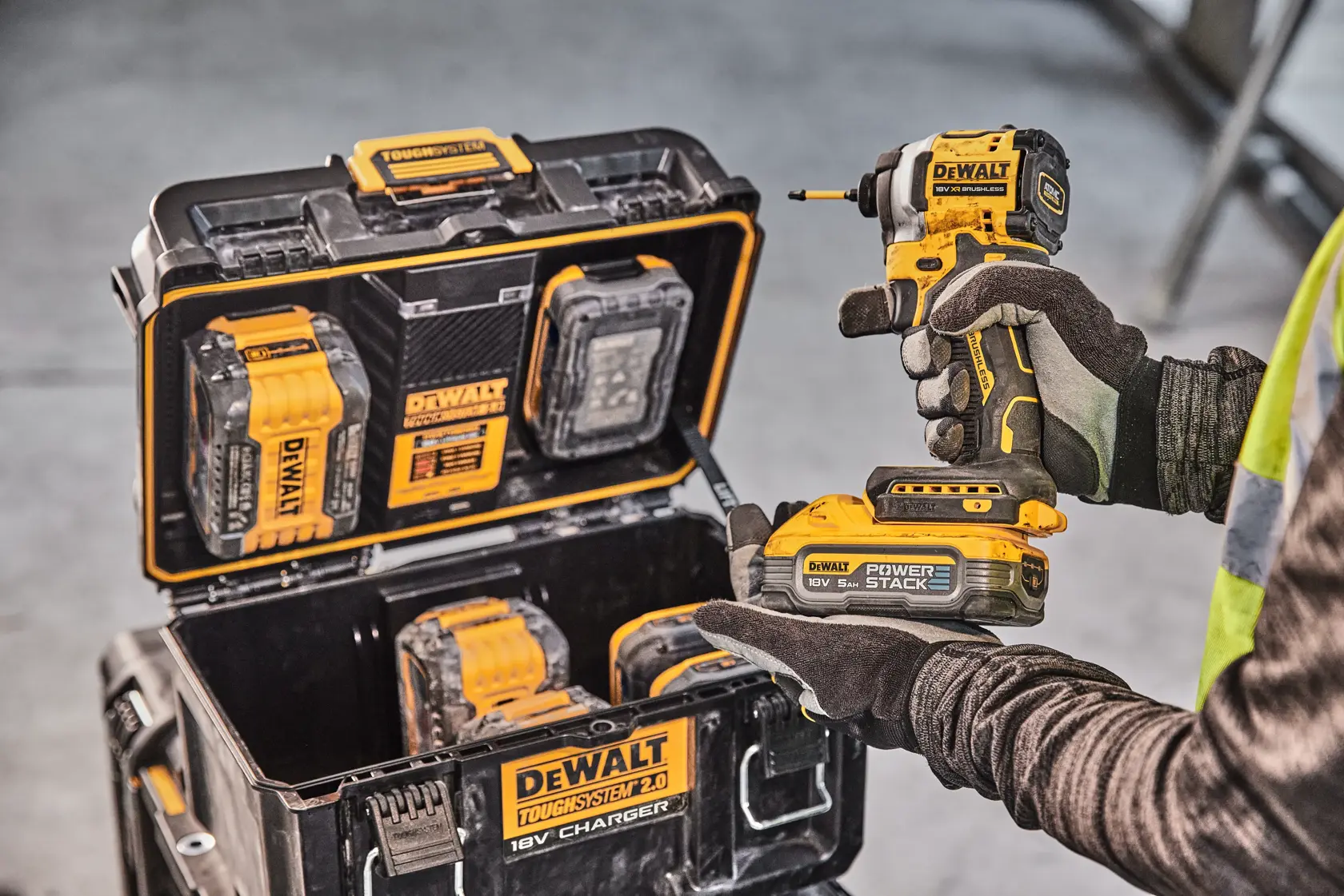 Persona con trapano DEWALT, valigia con batterie e utensili visibili. Ambiente industriale.