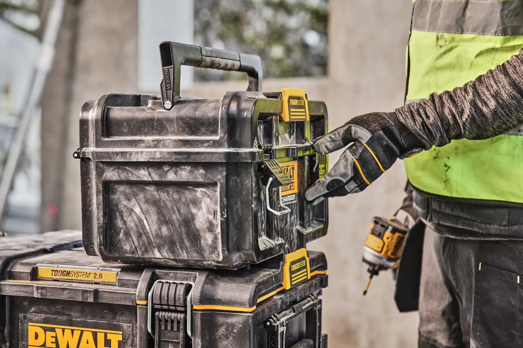 Mano con guanto apre una cassetta DEWALT Toughsystem 2.0 in un cantiere.