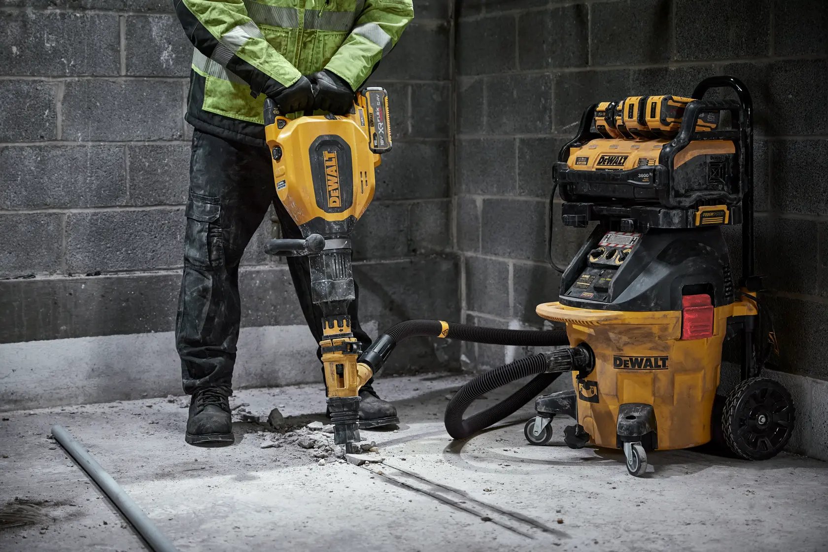 DEWALT worker uses a demolition hammer connected to a DWV905H dust extractor in a concrete room.