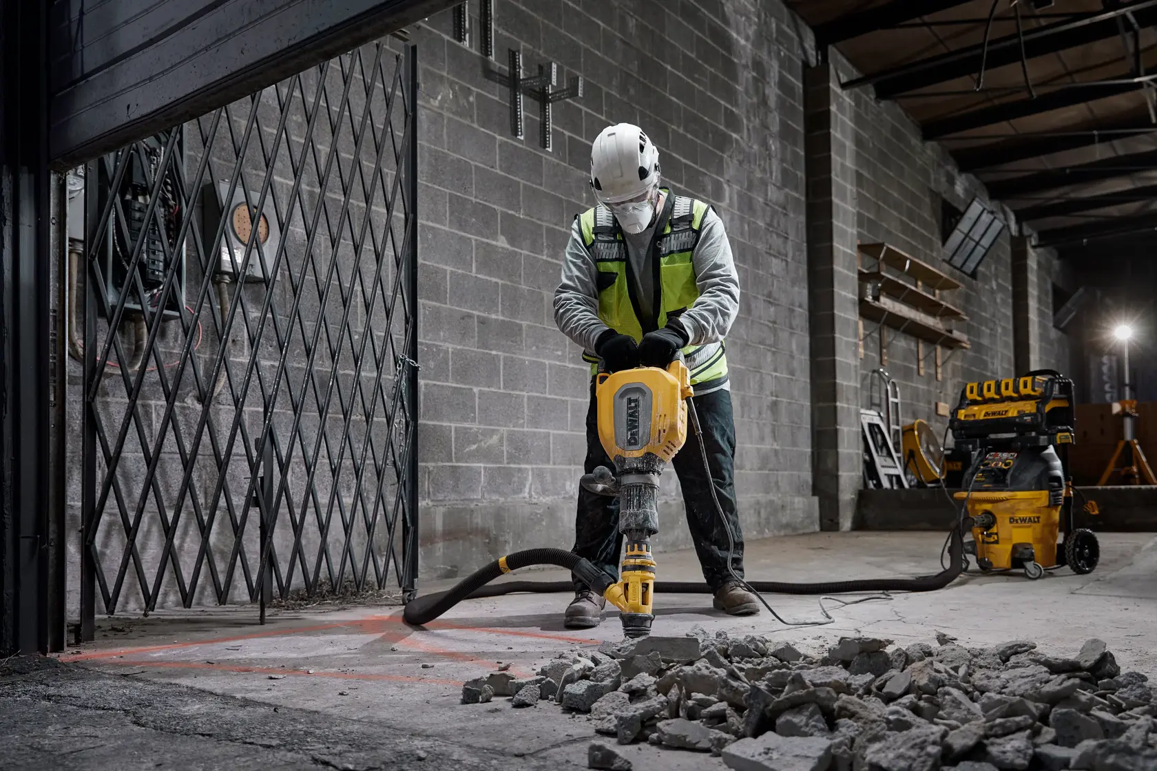 Worker uses DEWALT equipment to break concrete indoors. DEWALT vacuum system visible in background.